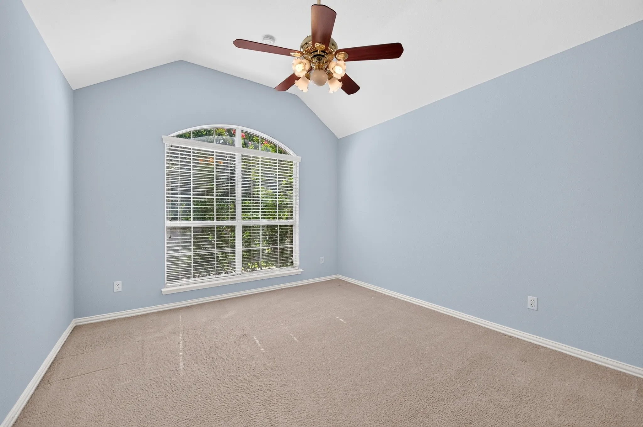 Vaulted ceiling room featuring an arched window, light blue wall paint, neutral carpet, and a ceiling fan