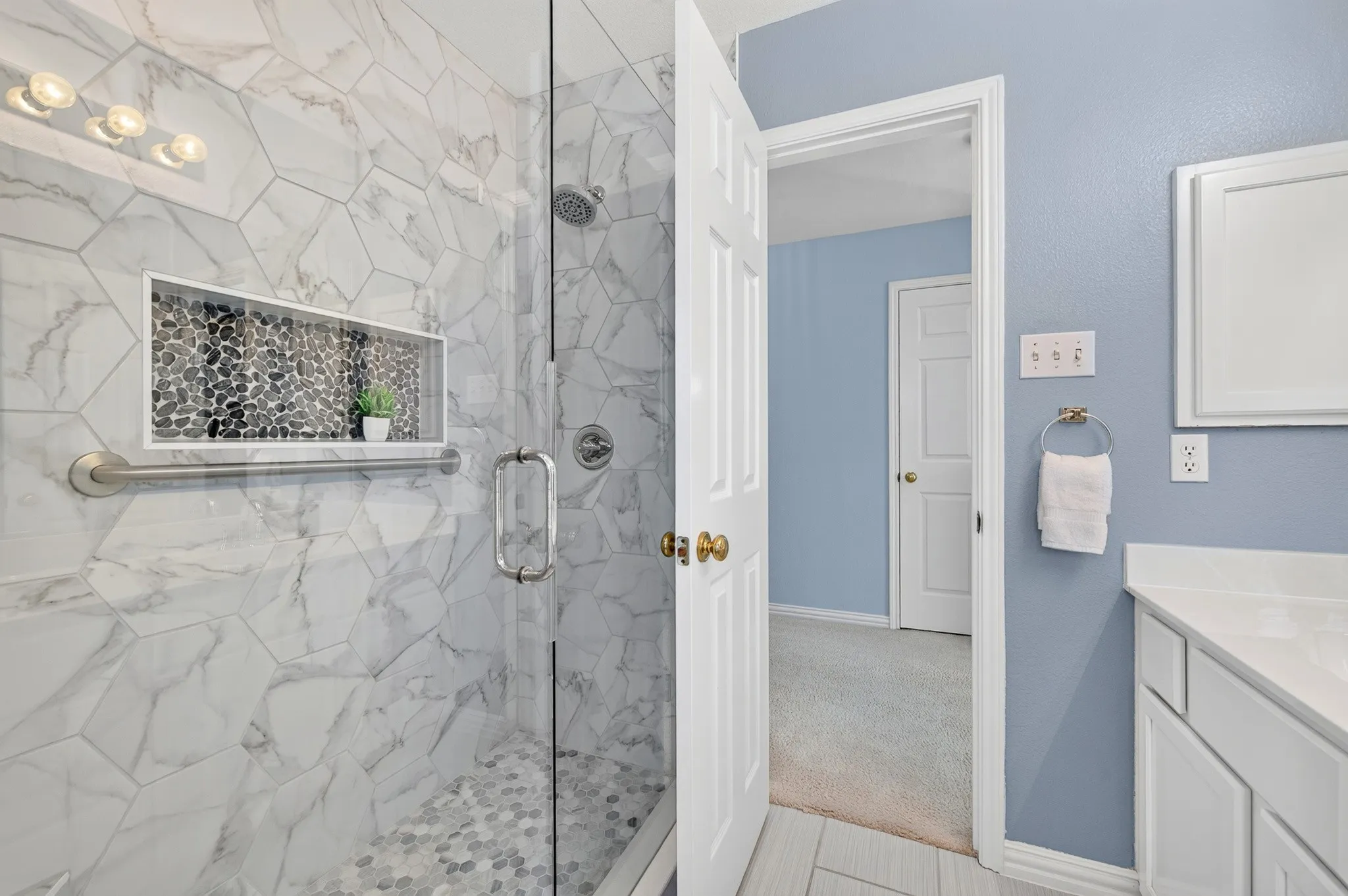 Glass-enclosed shower with hexagonal tile surround, built-in niche with pebble tile, and a rainfall showerhead