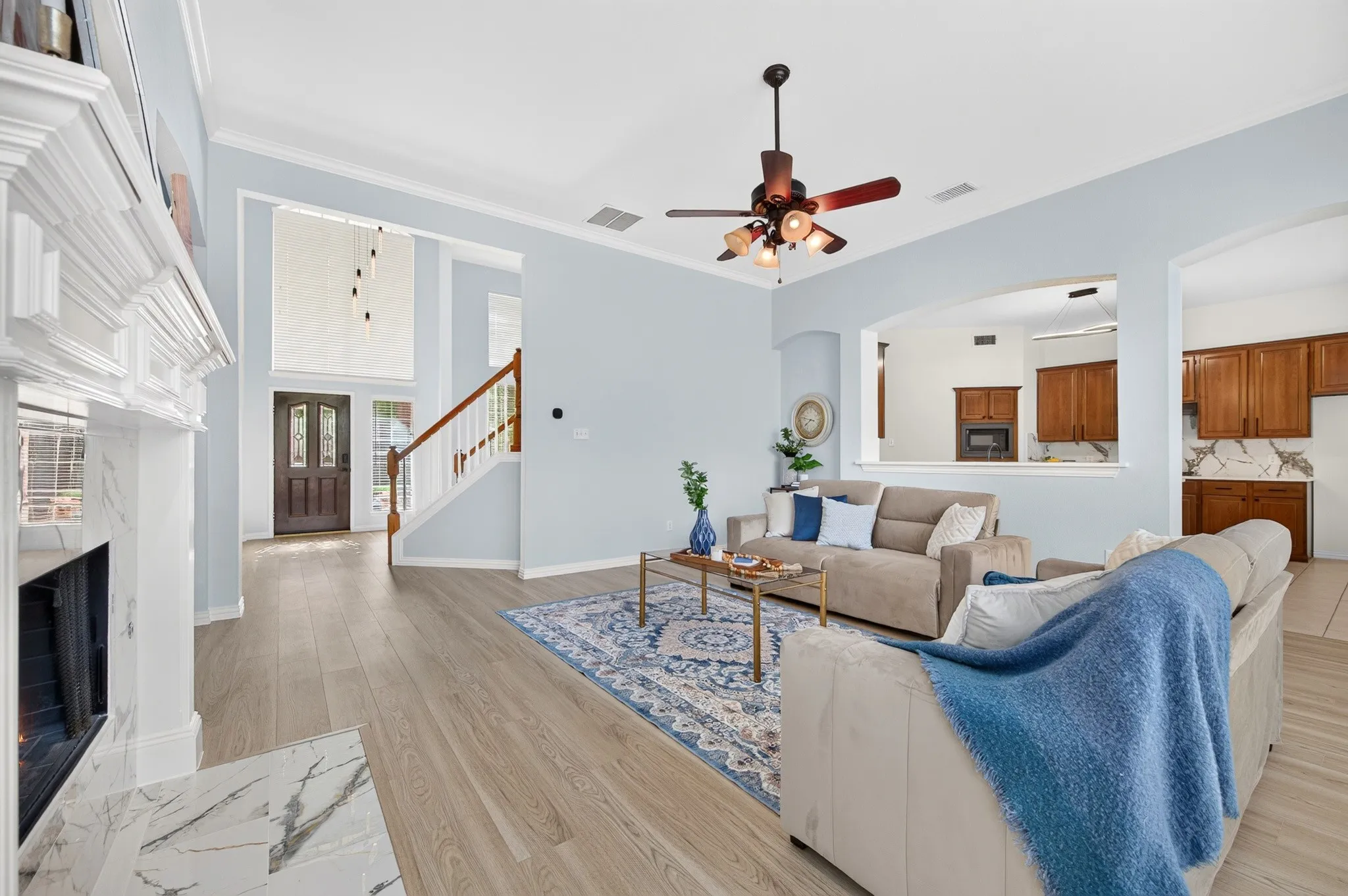 Living area featuring wood-finish flooring, a white mantel fireplace with a marble-style hearth, and a ceiling fan