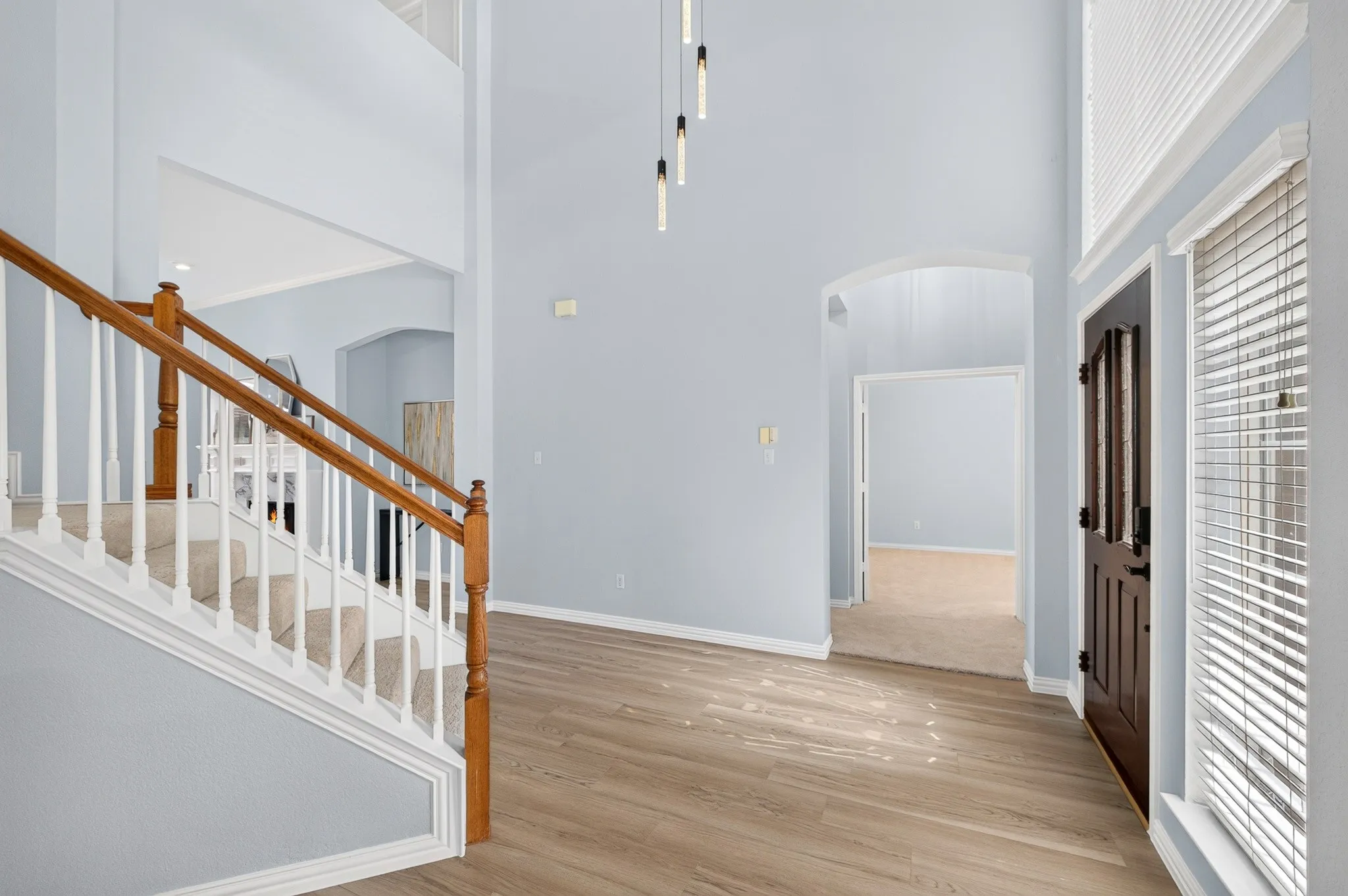 Foyer featuring wood-finish flooring, a carpeted staircase with wood handrails, a dark wood entry door with decorative glass, and a modern linear pendant light fixture