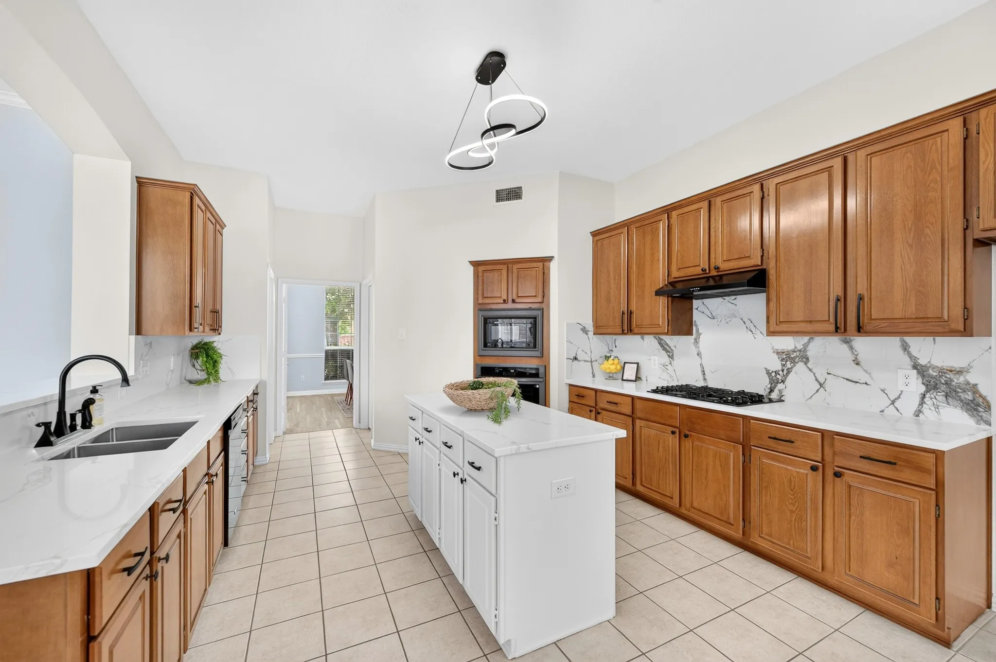 Kitchen featuring a central island, light wood cabinetry, white countertops, a gas cooktop, and tile flooring