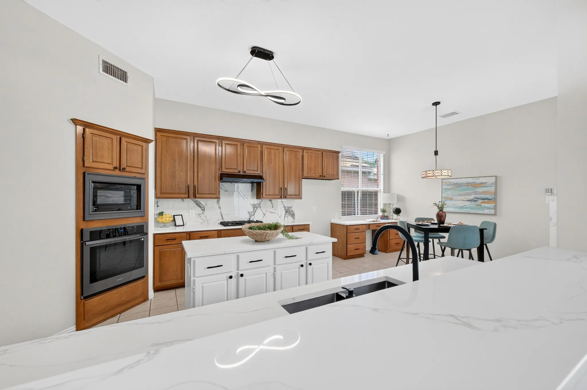 Kitchen featuring white countertops, a central island with white cabinetry, brown wall and base cabinets, a built-in microwave and oven, and a contemporary pendant light fixture