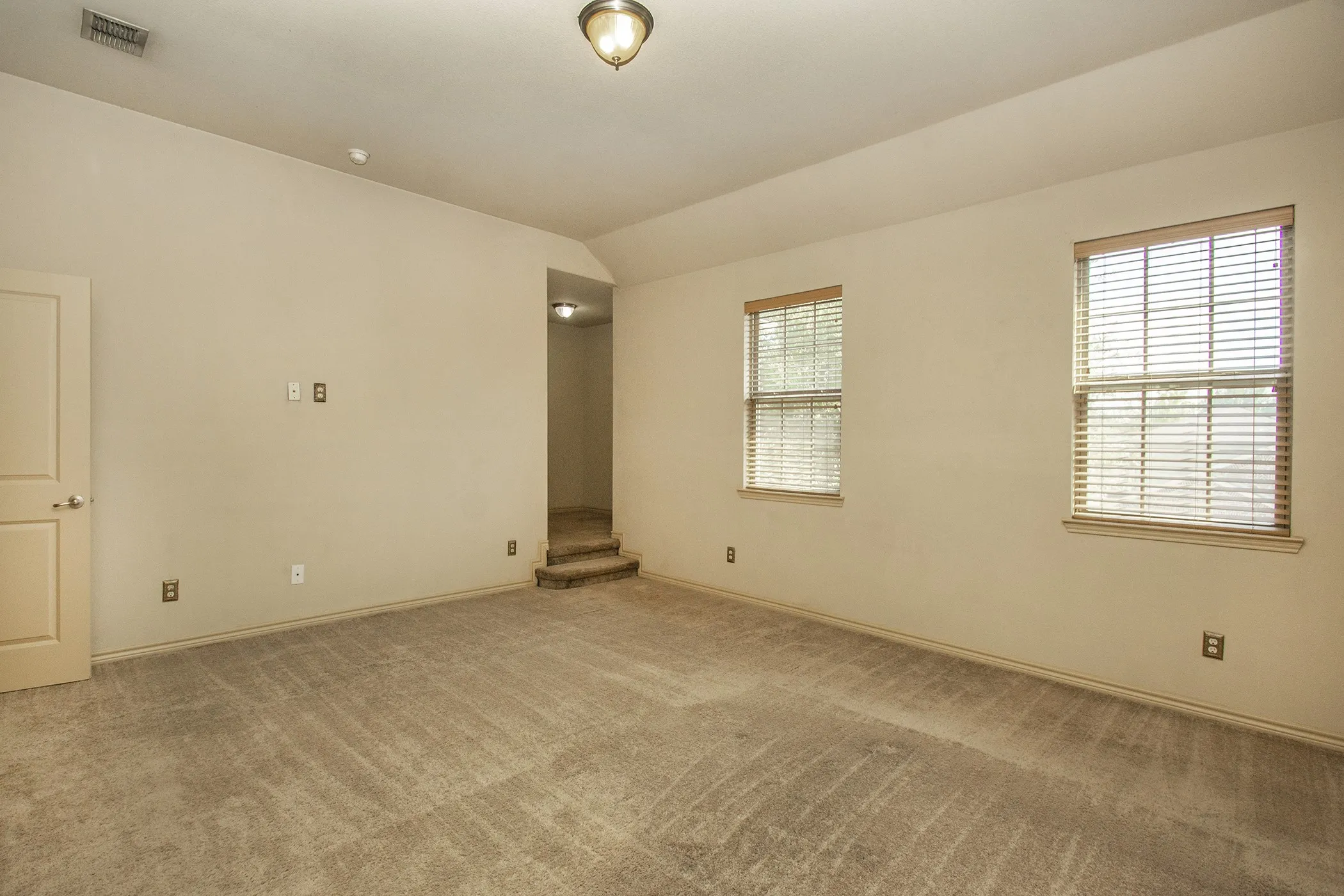 Steps to Primary Bedroom from The Family Room with Neutral wall paint, two windows with blinds, carpeted flooring, and a ceiling-mounted light fixture