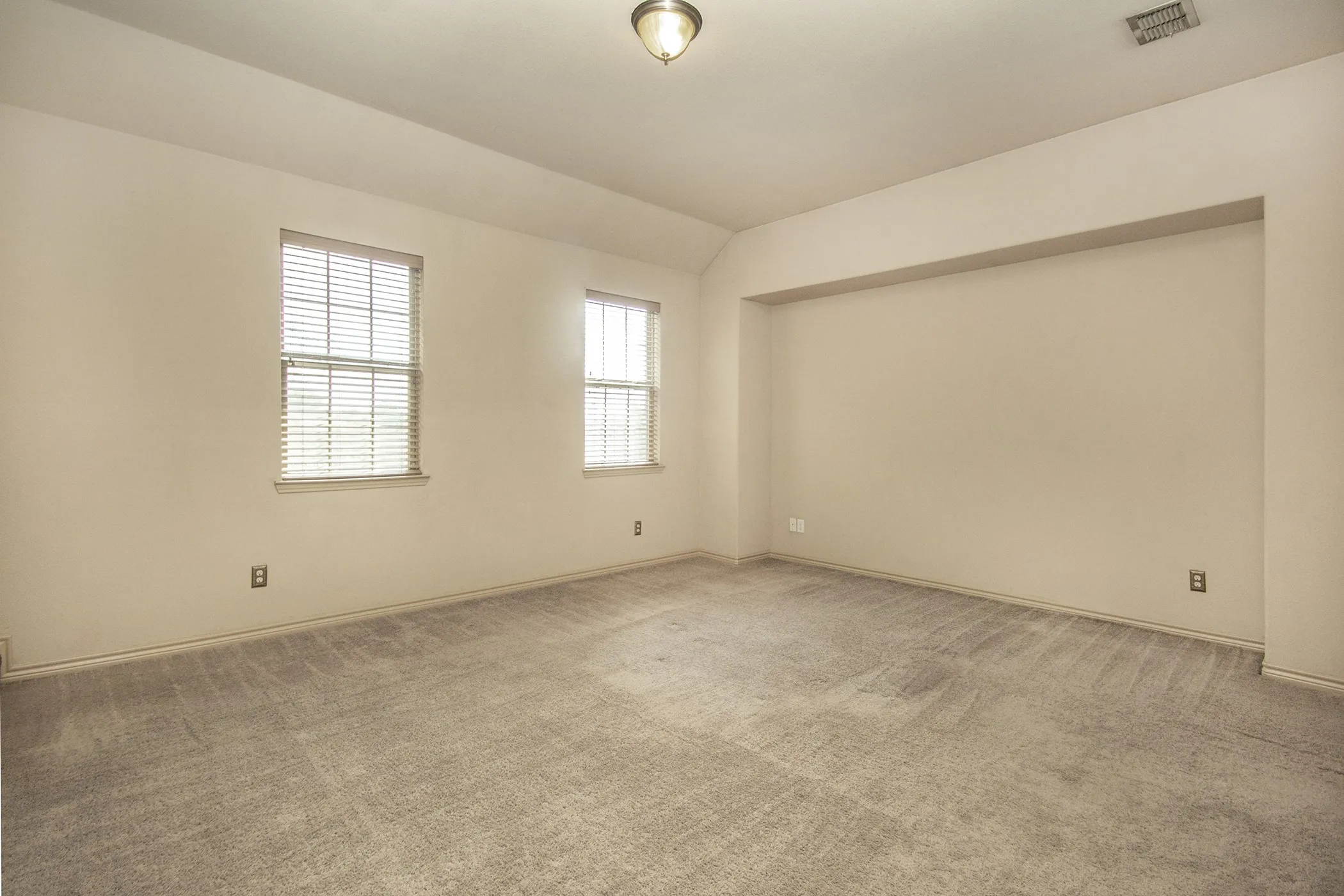 Recessed wall niche, sloped ceiling, two windows with blinds, and neutral carpeting