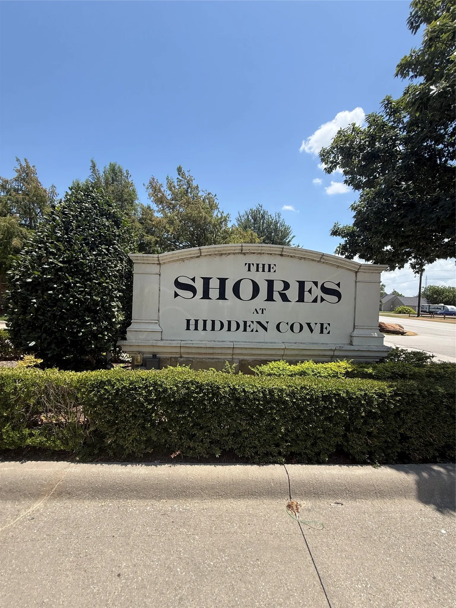 Community entrance "The Shores at Hidden Cove" with manicured shrubbery and mature landscaping