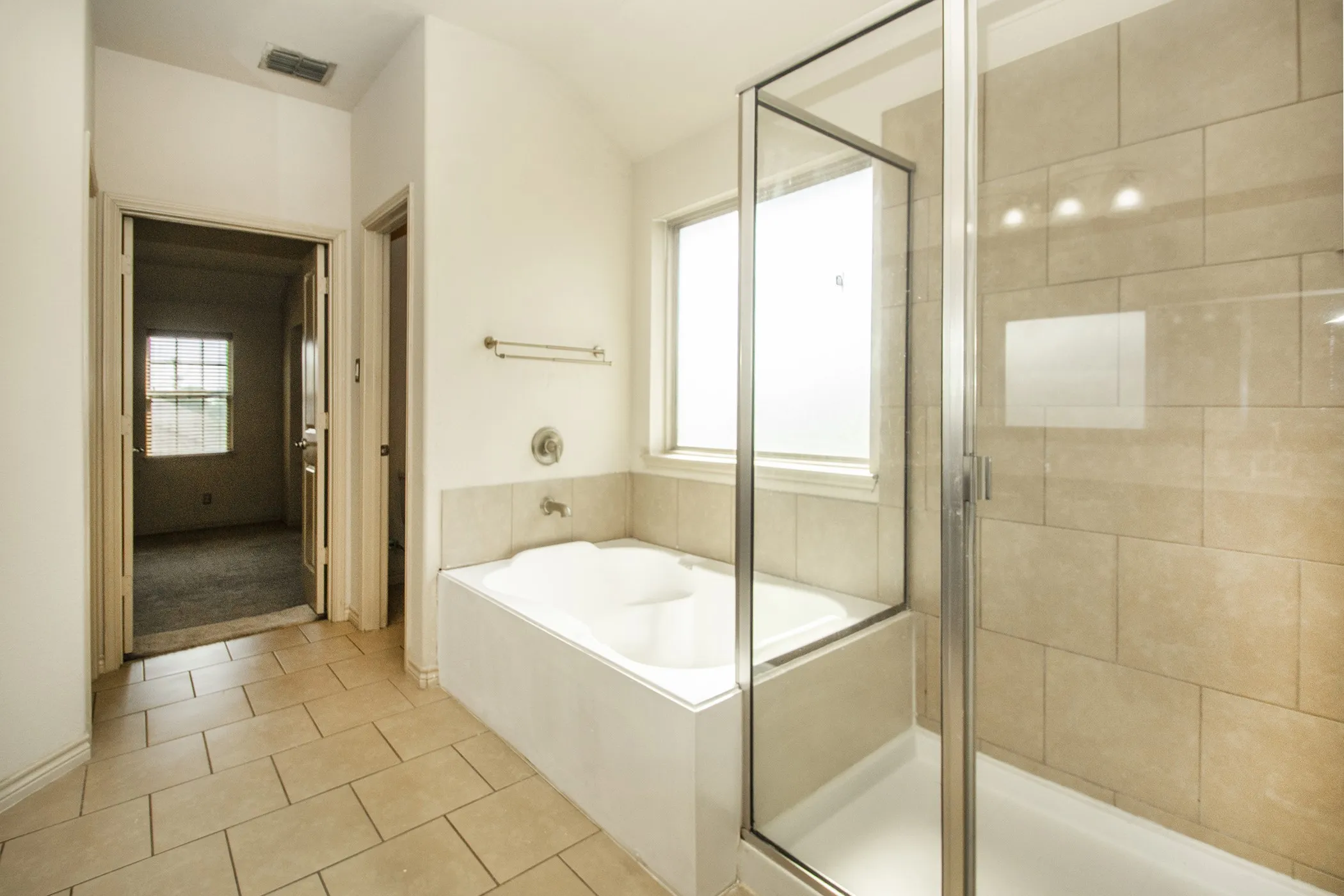 Soaking tub with a tiled surround, separate glass-enclosed shower, and neutral tile flooring