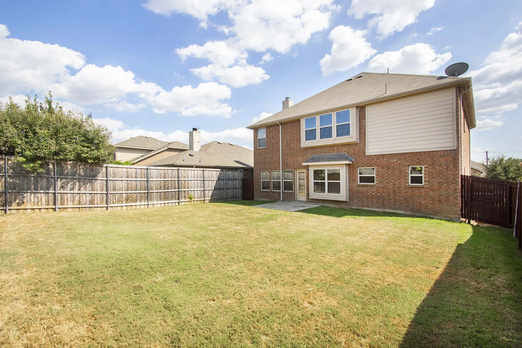Expansive lawn with wood privacy fencing, brick exterior, and multiple windows
