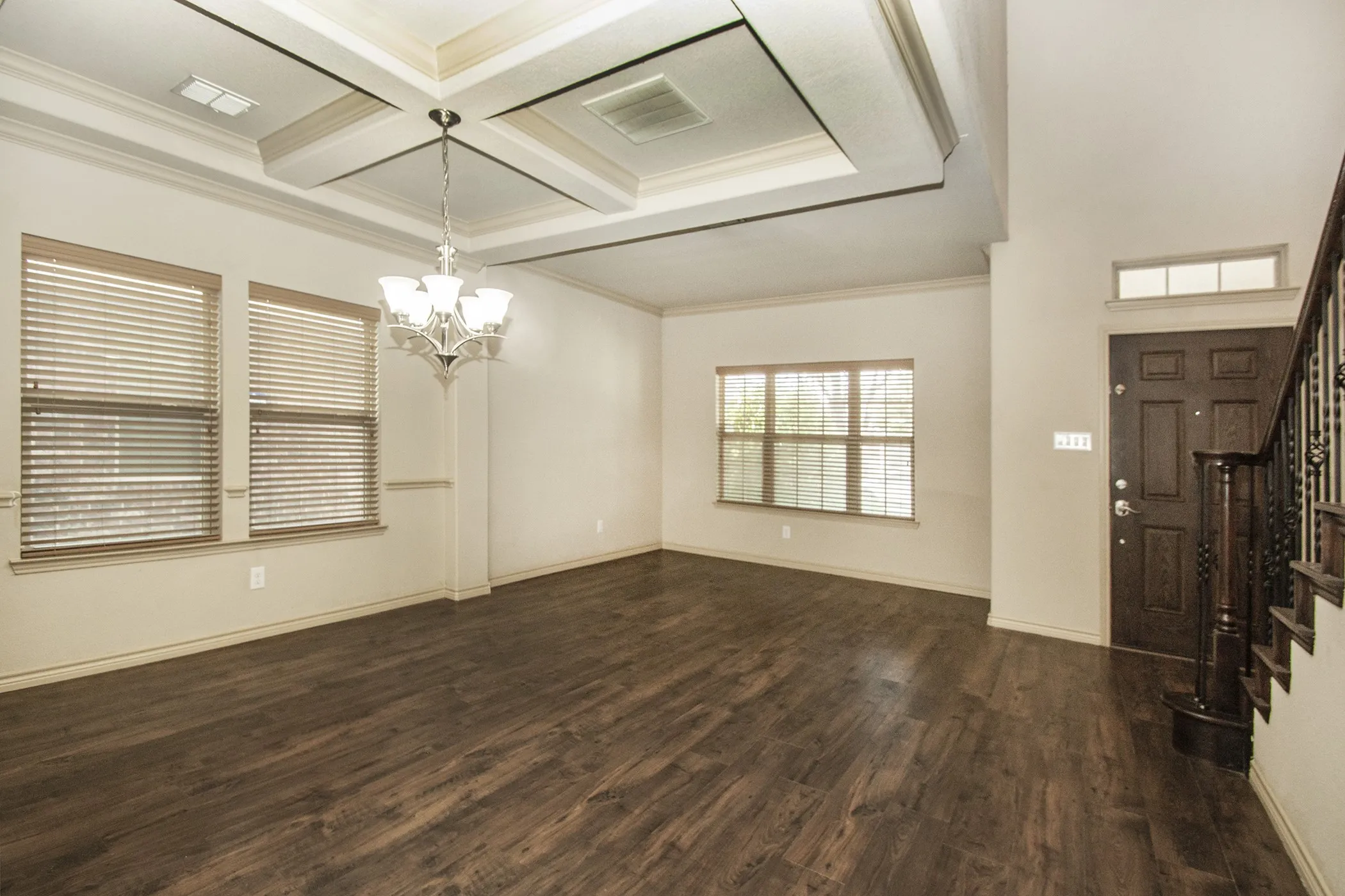 Tray ceiling with decorative moldings, chandelier, wood-finish flooring, multiple windows, and a dark wood front door