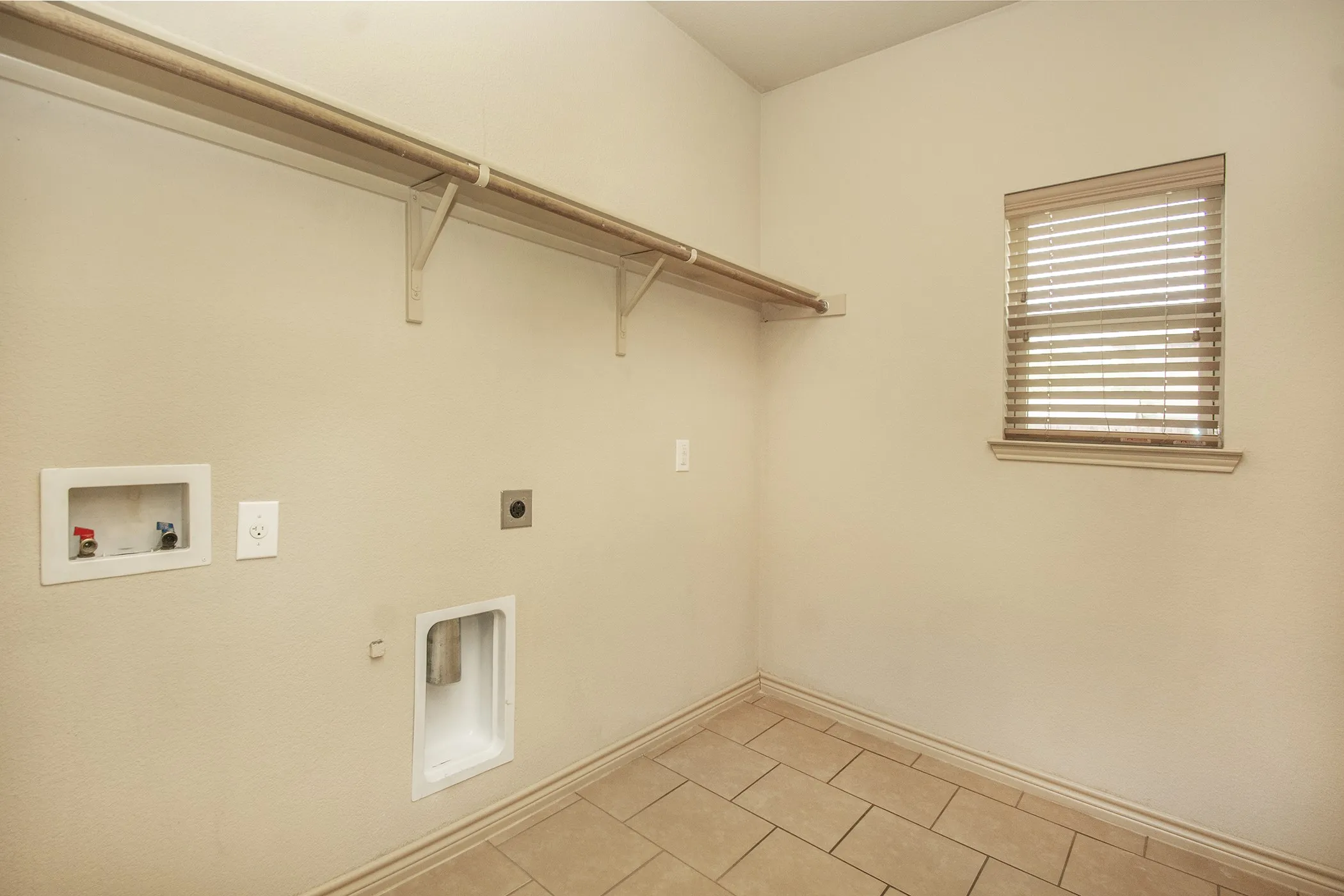 Tiled flooring, wall-mounted shelving, window with blinds, and utility connections