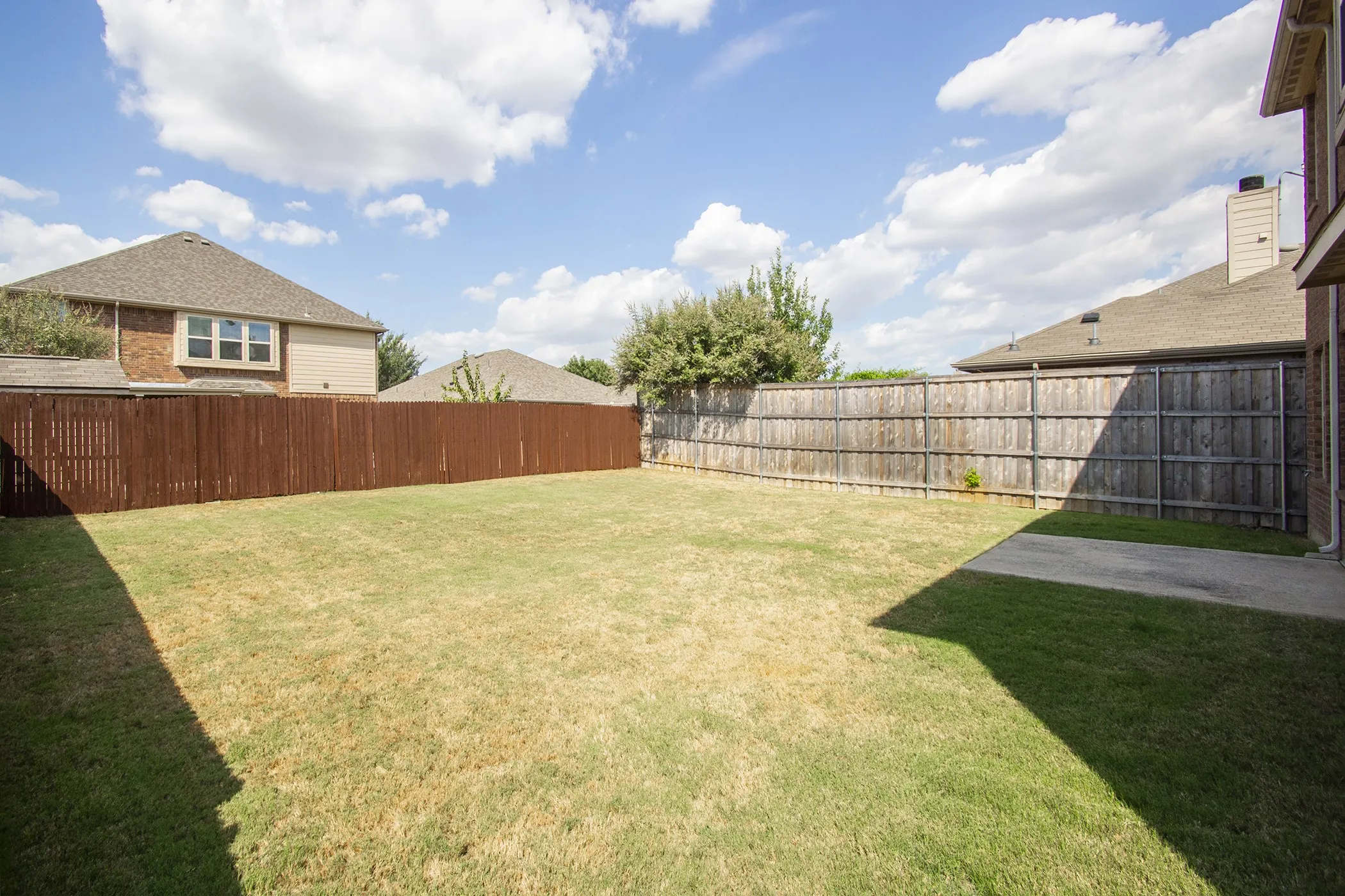 Fenced backyard with a combination of wood and stained wood fencing, featuring a concrete patio