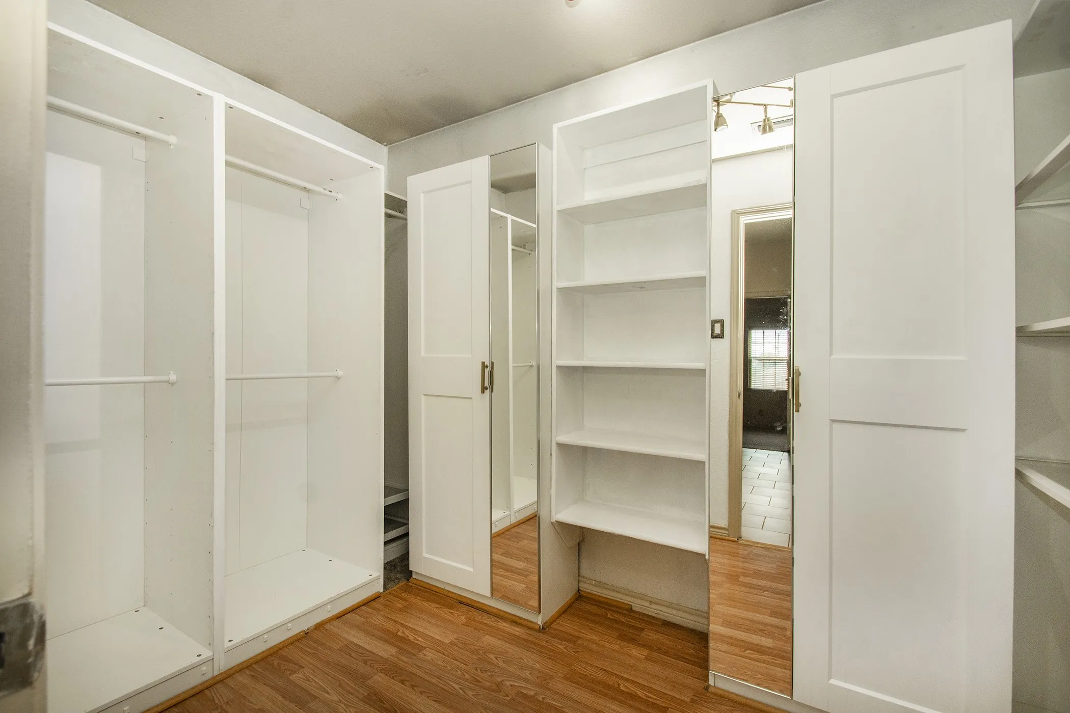 Extra-Large Primary Bedroom Closet with Integrated white closet cabinetry with a mirrored panel and wood-finish flooring