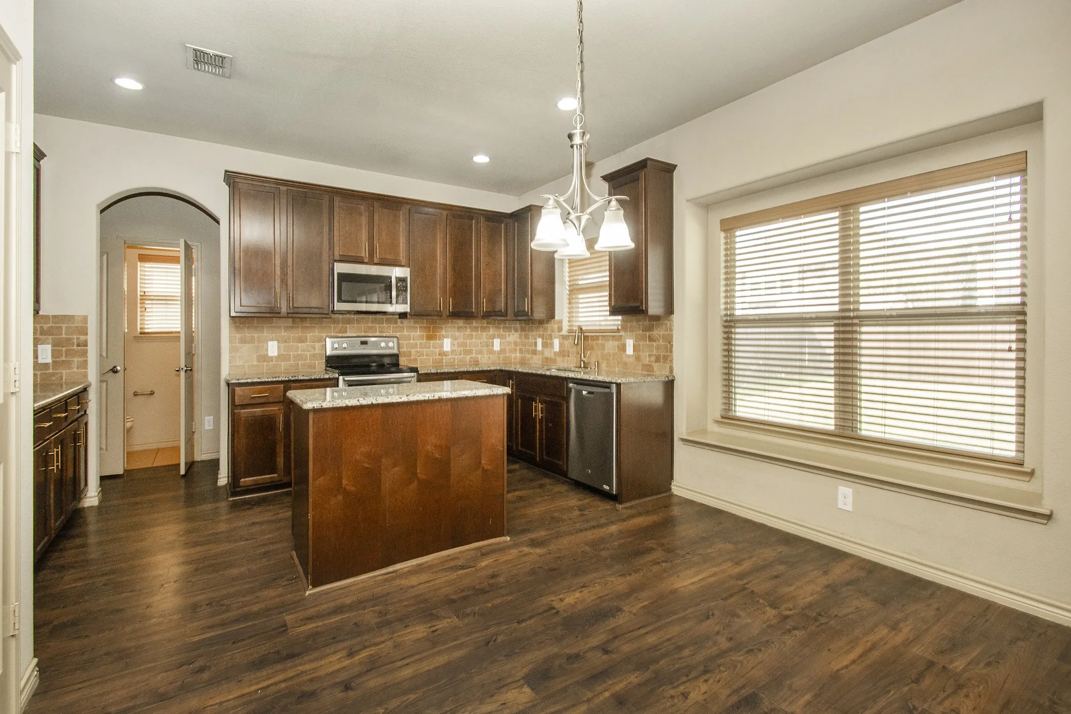 Kitchen featuring wood-finish flooring, dark wood cabinetry, stainless steel appliances, a center island with a stone countertop, and a tiled backsplash