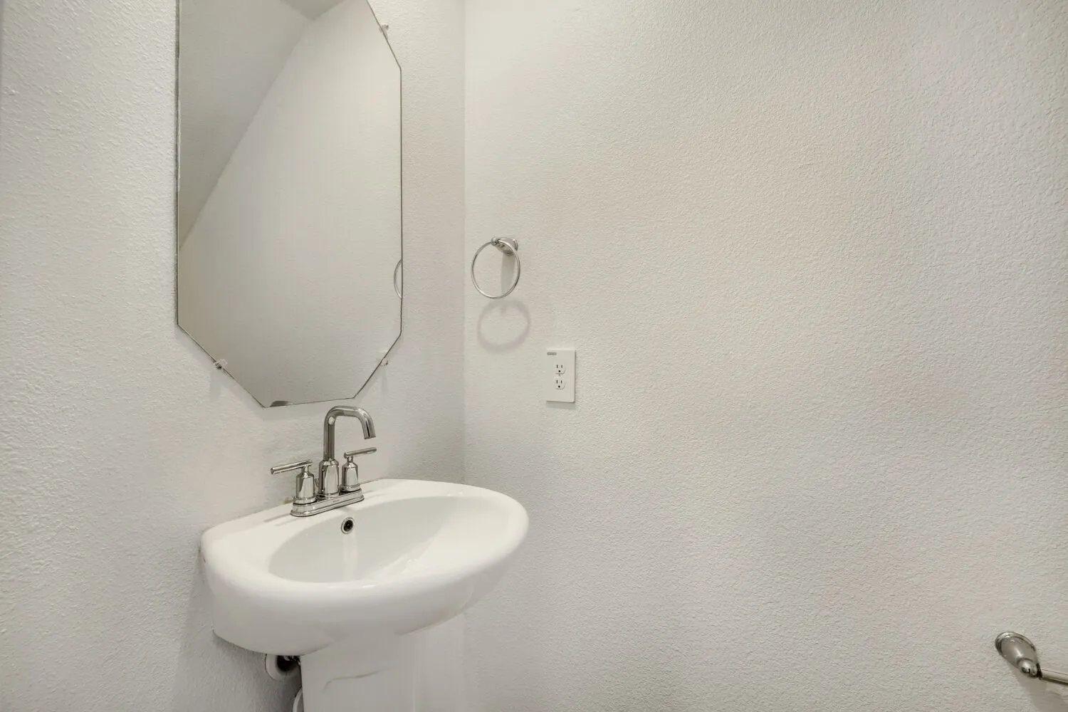 Pedestal sink with chrome faucet, octagonal wall mirror, and textured white wall finish