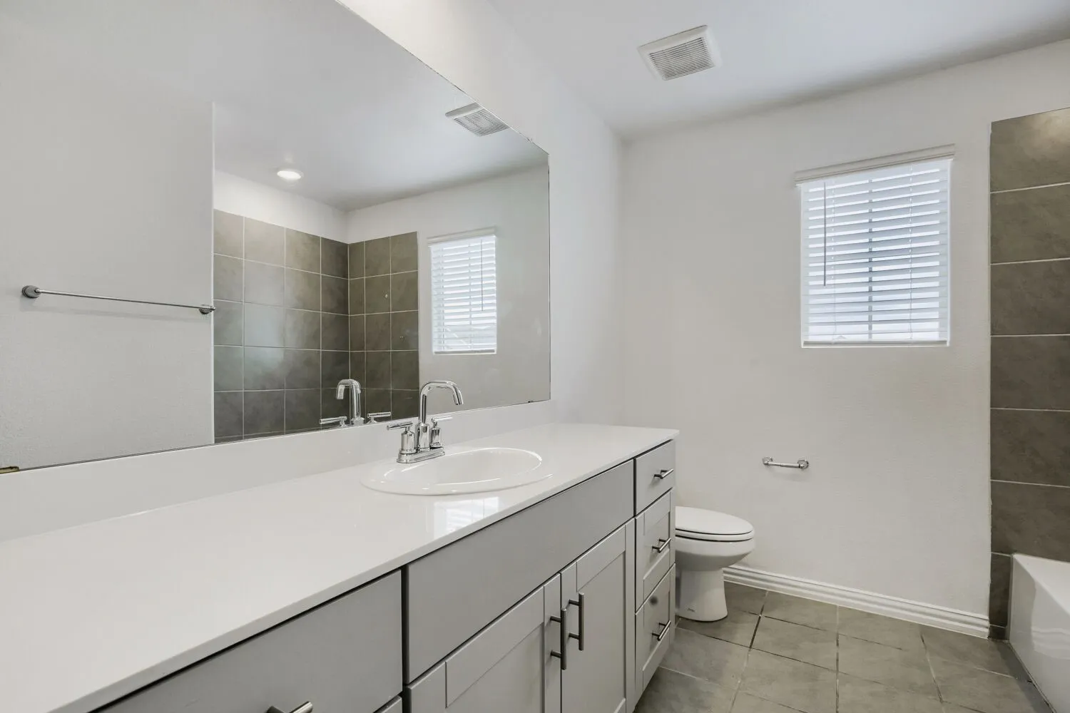 Bathroom featuring a light gray vanity with a single basin sink, chrome faucet, and white countertop
