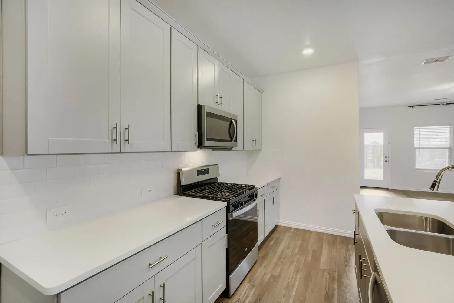 Contemporary kitchen featuring light gray cabinetry, white countertops, a subway tile backsplash, and stainless steel appliances