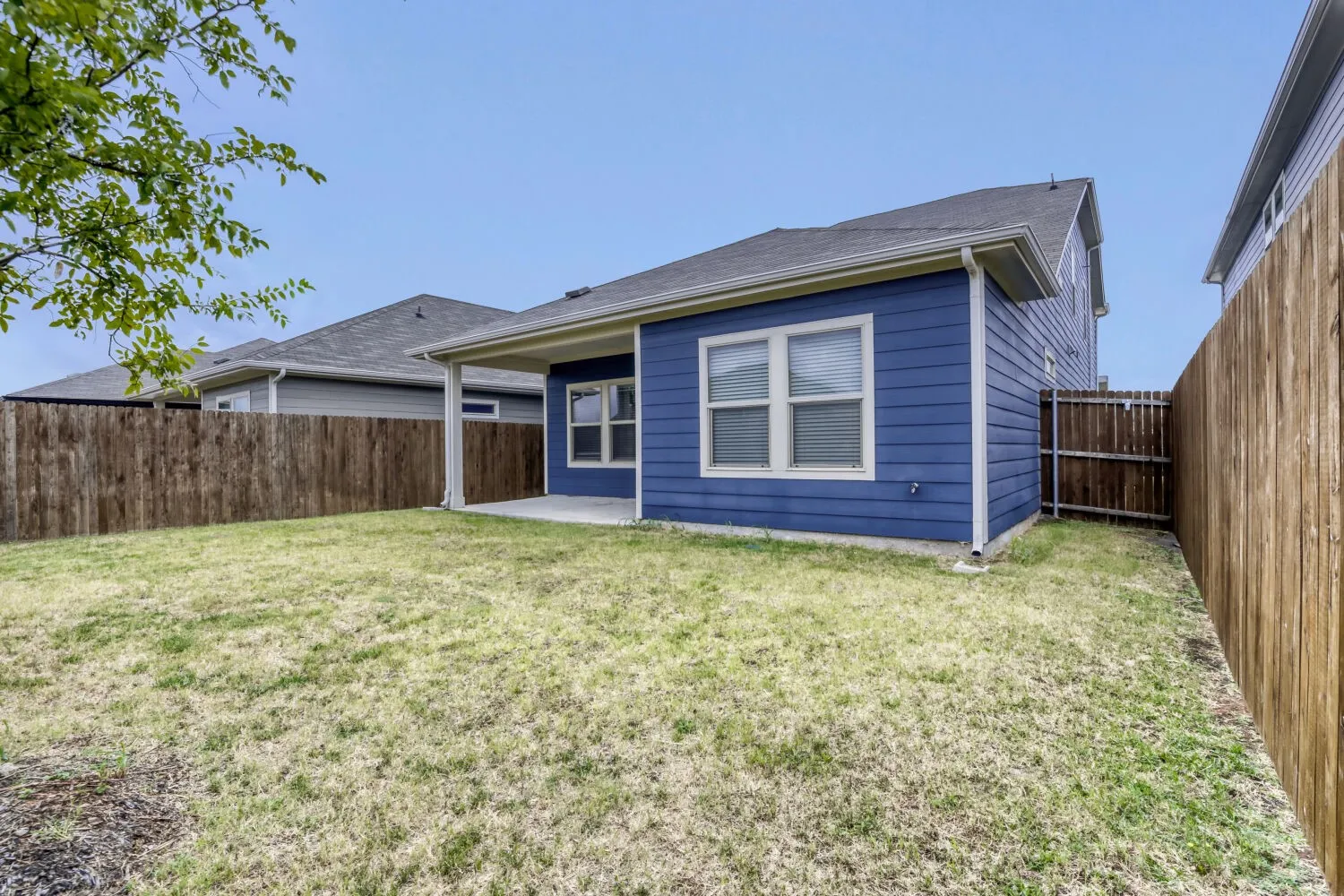 Expansive backyard with a covered patio, blue siding, a wooden privacy fence, and a green lawn area
