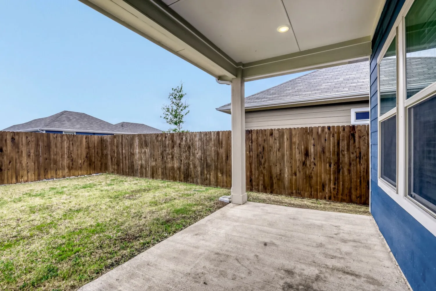 Expansive covered patio with concrete flooring, recessed lighting, and a vibrant blue exterior wall