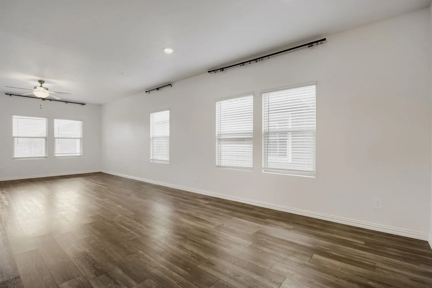 Spacious interior room featuring wood-finish flooring, multiple windows with blinds, recessed lighting, and a ceiling fan
