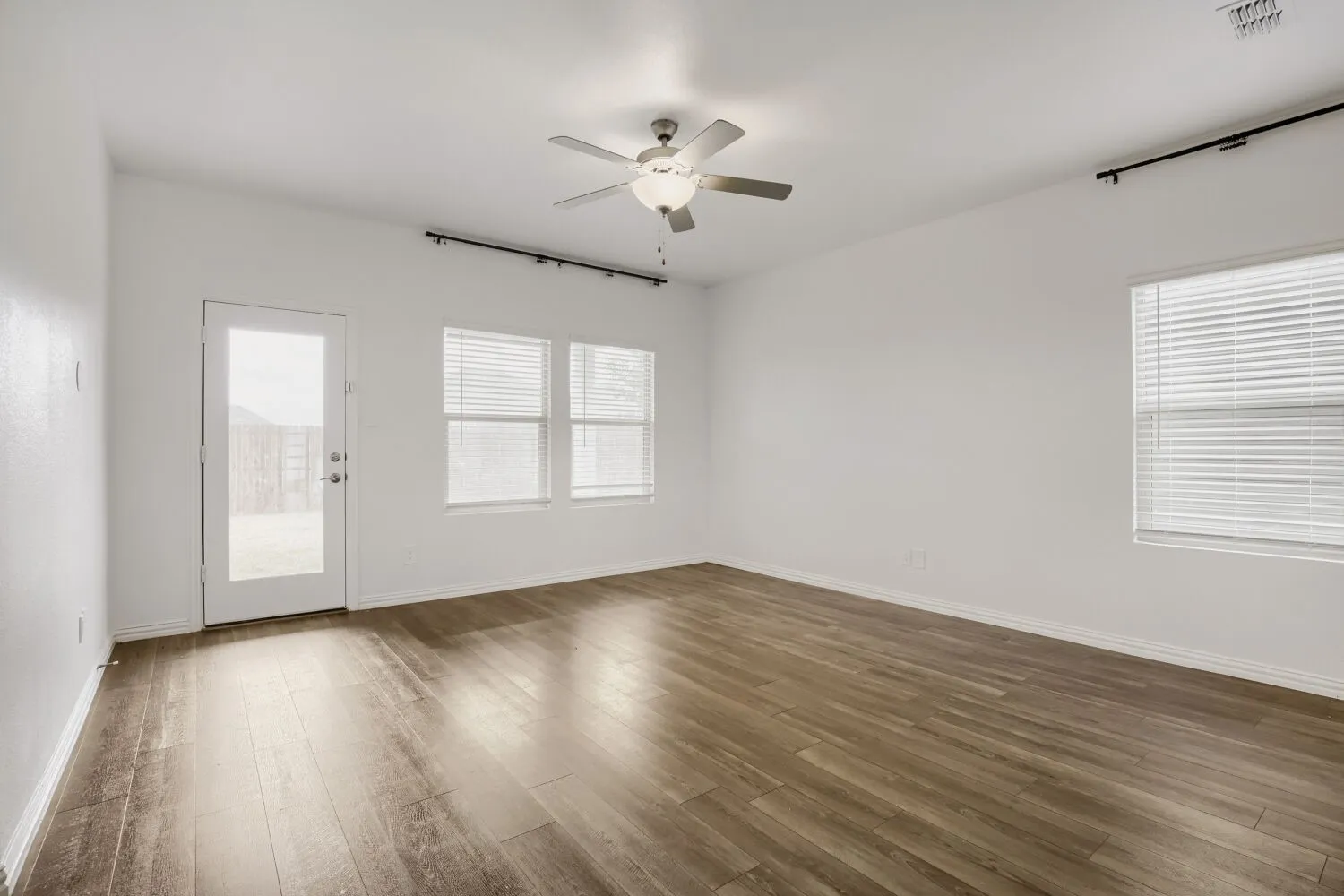 Spacious room featuring wood-finish flooring, white walls, and multiple windows with blinds