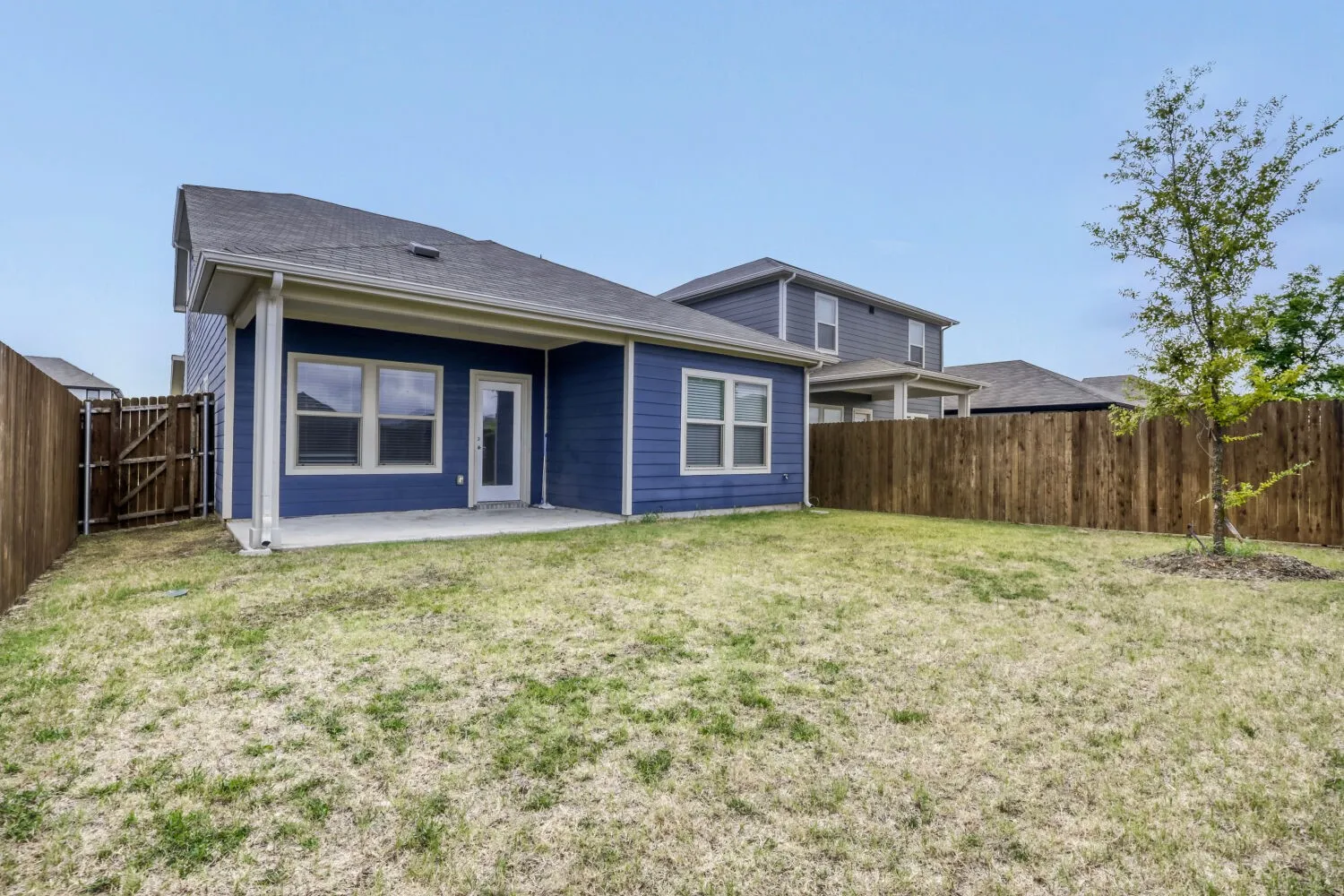 Spacious backyard featuring a covered concrete patio, wood privacy fencing, and a mature tree