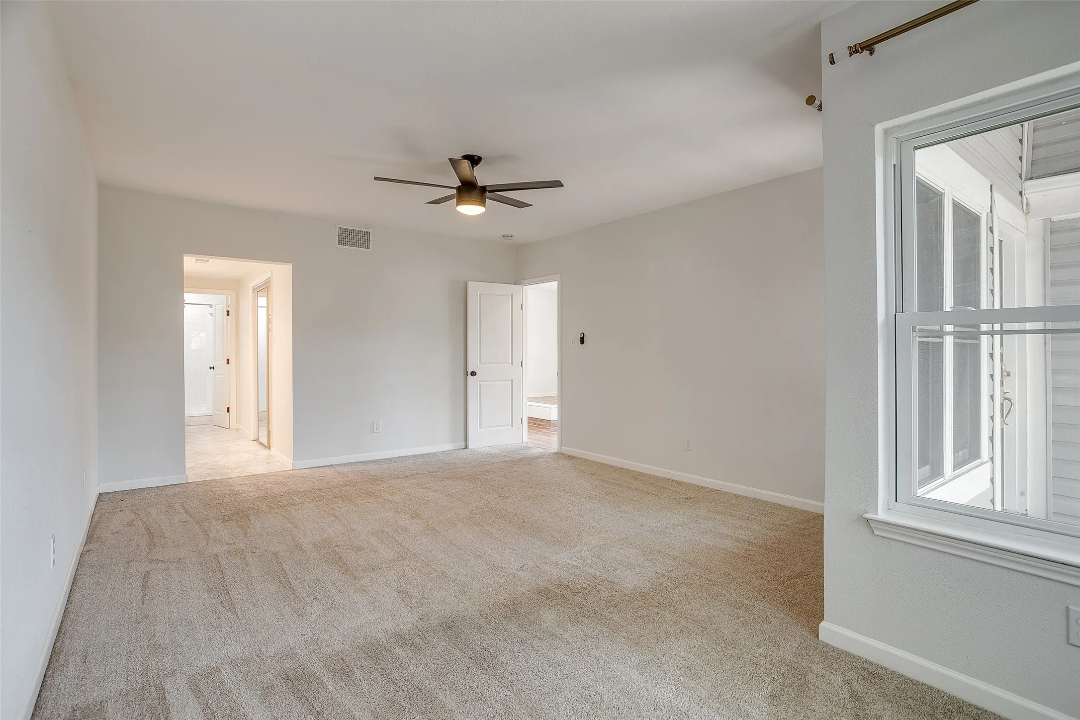 Primary bedroom with carpet, ceiling fan, and natural light.