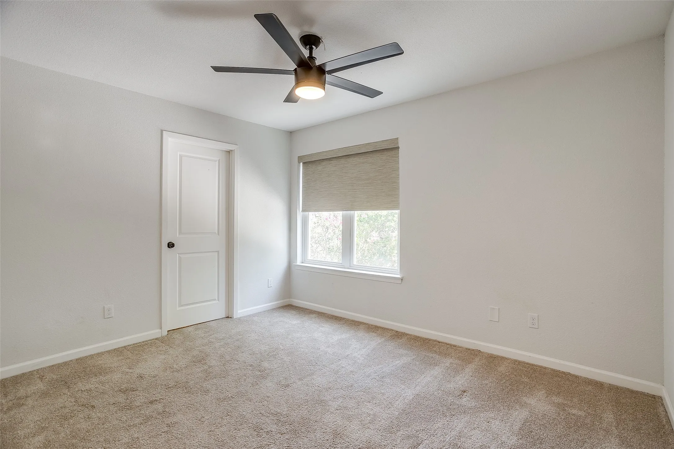 Second bedroom with carpet, ceiling fan, and bright window.