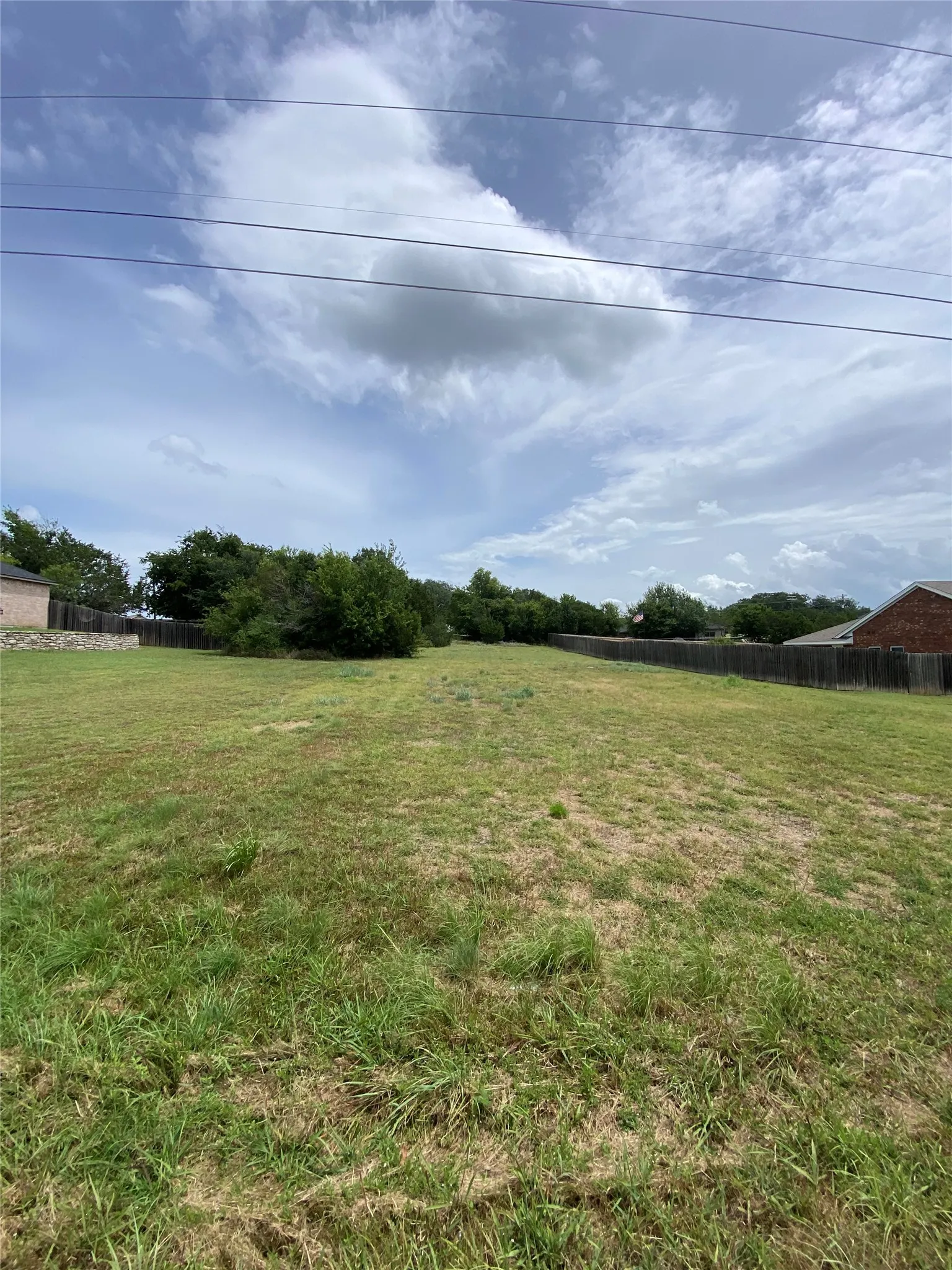 Expansive cleared lot featuring partial wood fencing and mature trees along the perimeter