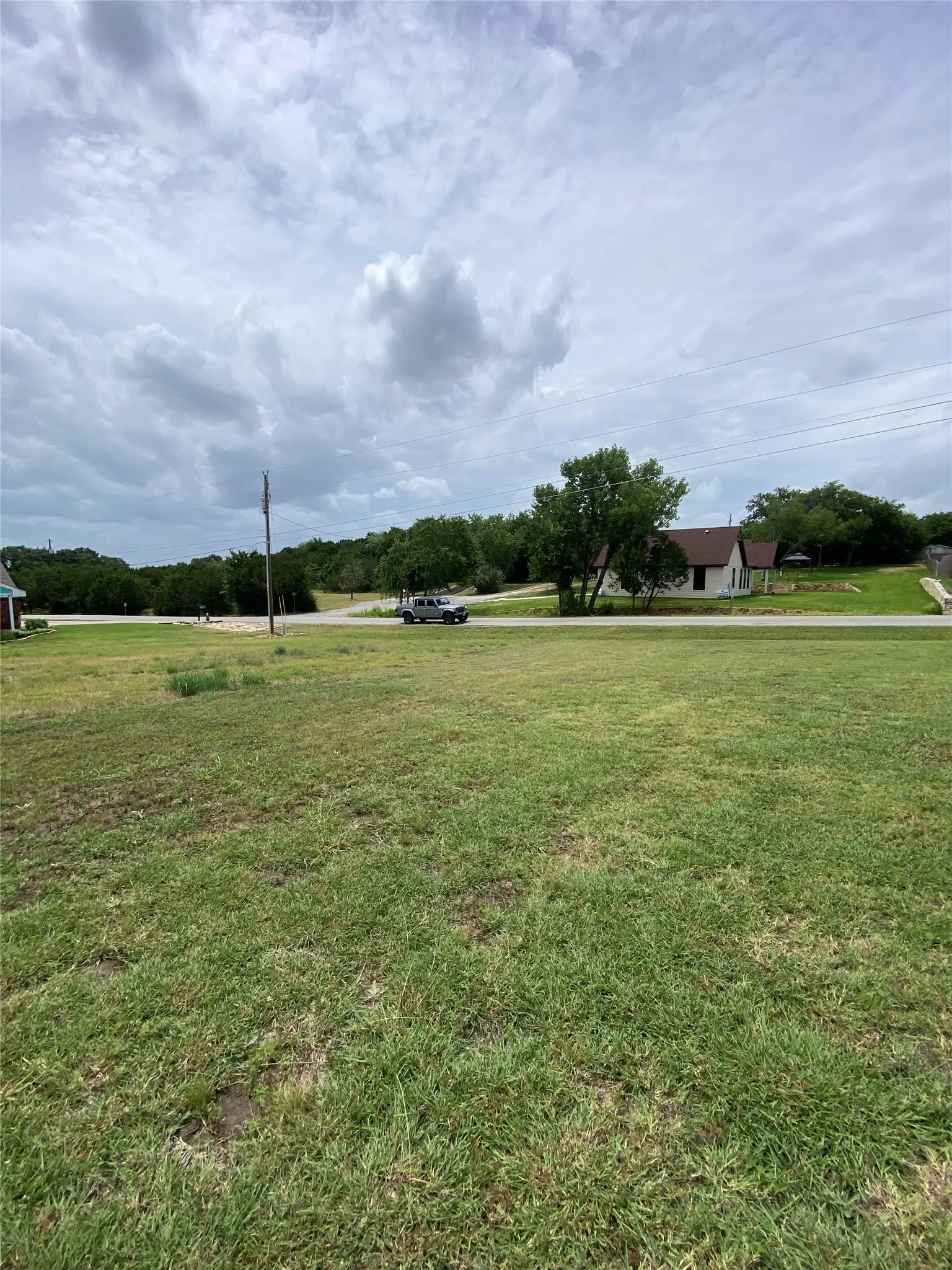 Expansive green space featuring a large grassy area, distant trees, and a partially visible residential structure