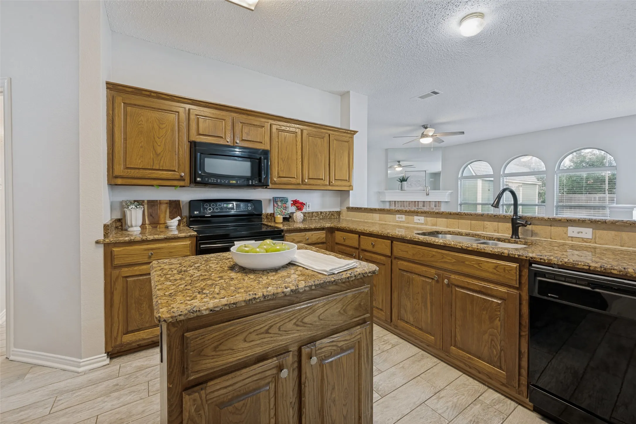 Kitchen featuring wood cabinetry, granite countertops, black appliances, and a central island