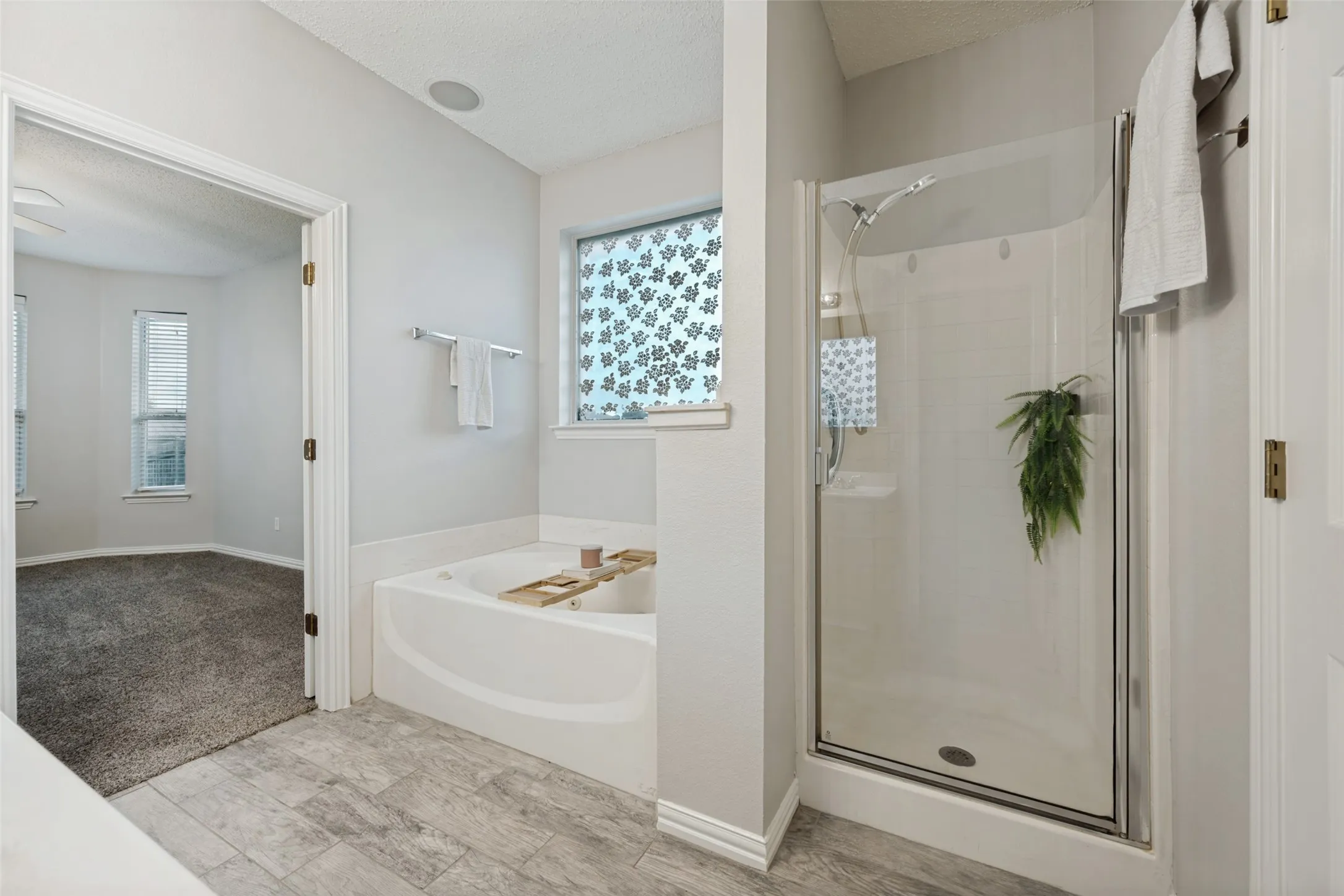 Bathroom featuring a corner soaking tub, a glass-enclosed shower, and wood-finish tile flooring
