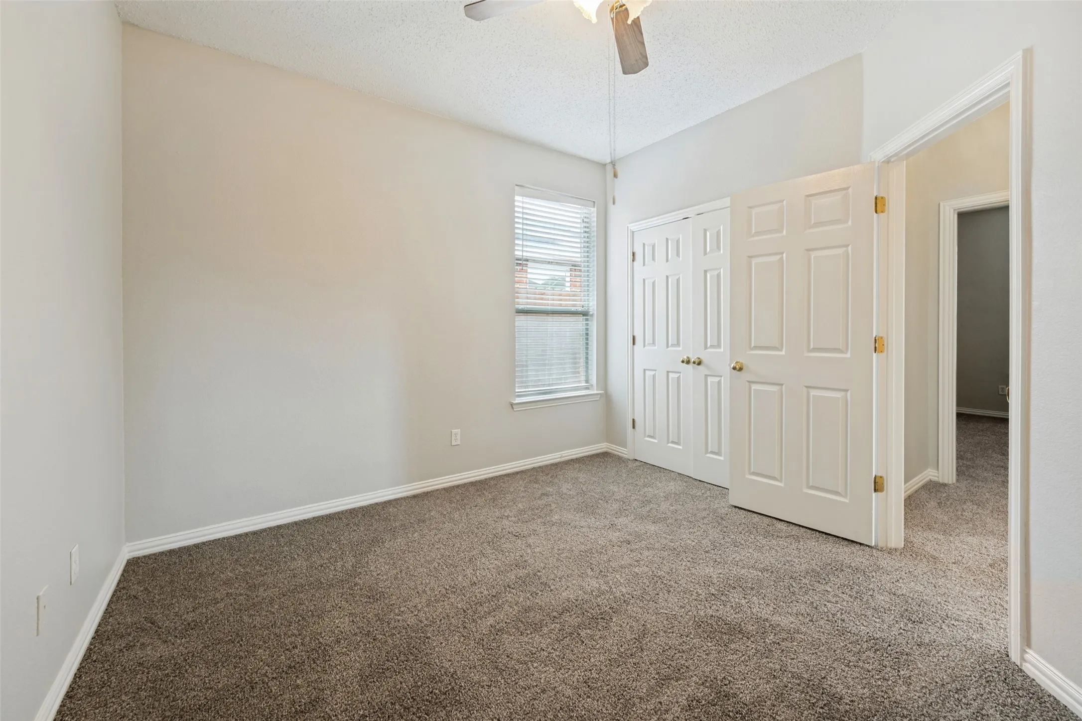 Carpeted room featuring a ceiling fan, window with blinds, and white bi-fold closet doors