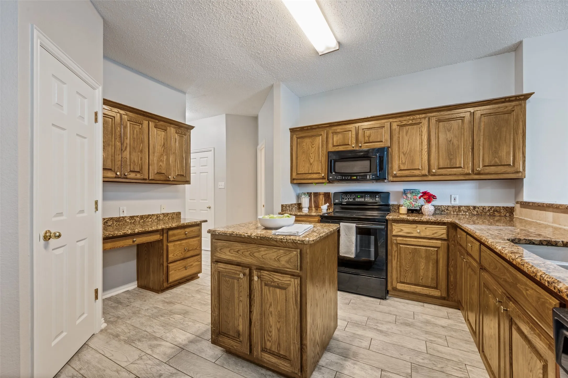 Kitchen featuring wood cabinetry, granite-style countertops with a matching backsplash, a central island, and black appliances