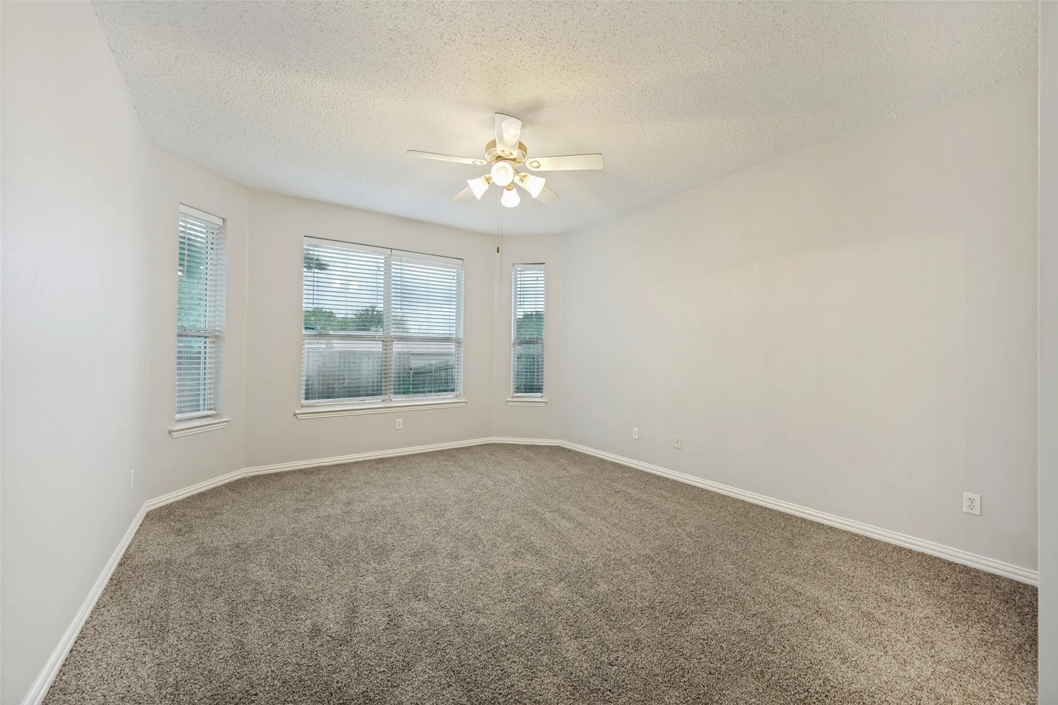 Spacious room featuring neutral carpeting, light-toned walls, and a multi-light ceiling fan