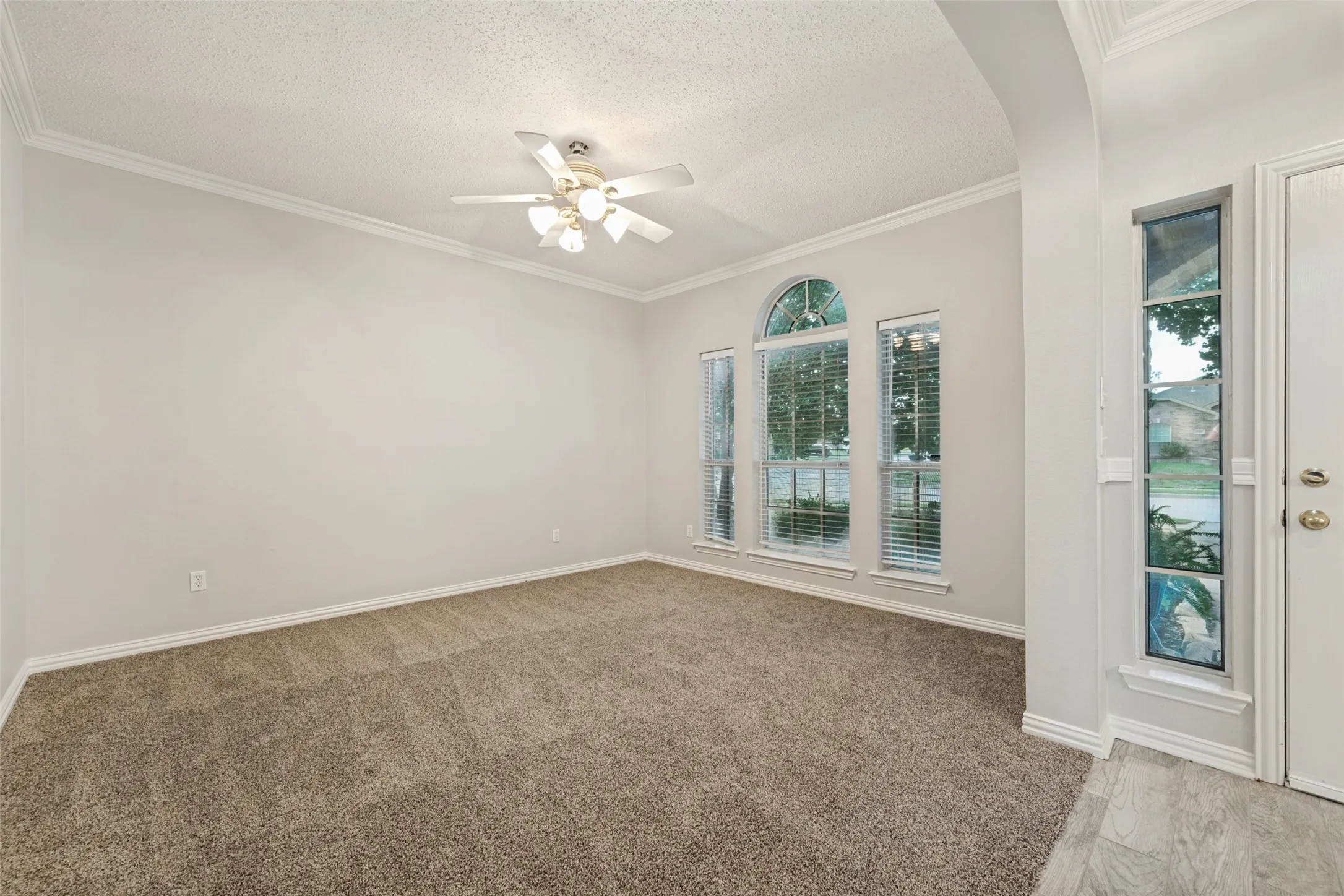 Carpeted interior space featuring a ceiling fan, crown molding, and multiple windows including an arched design
