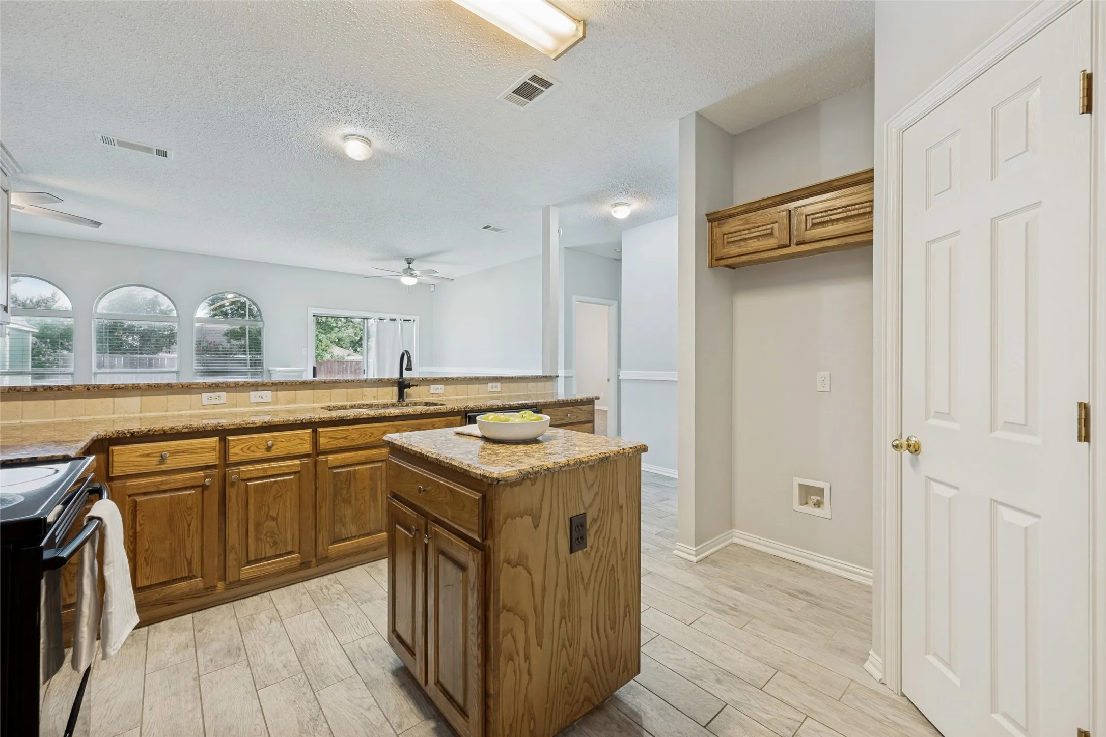 Kitchen featuring wood-finish cabinetry, granite-style countertops, a tiled backsplash, and light wood-grain tile flooring