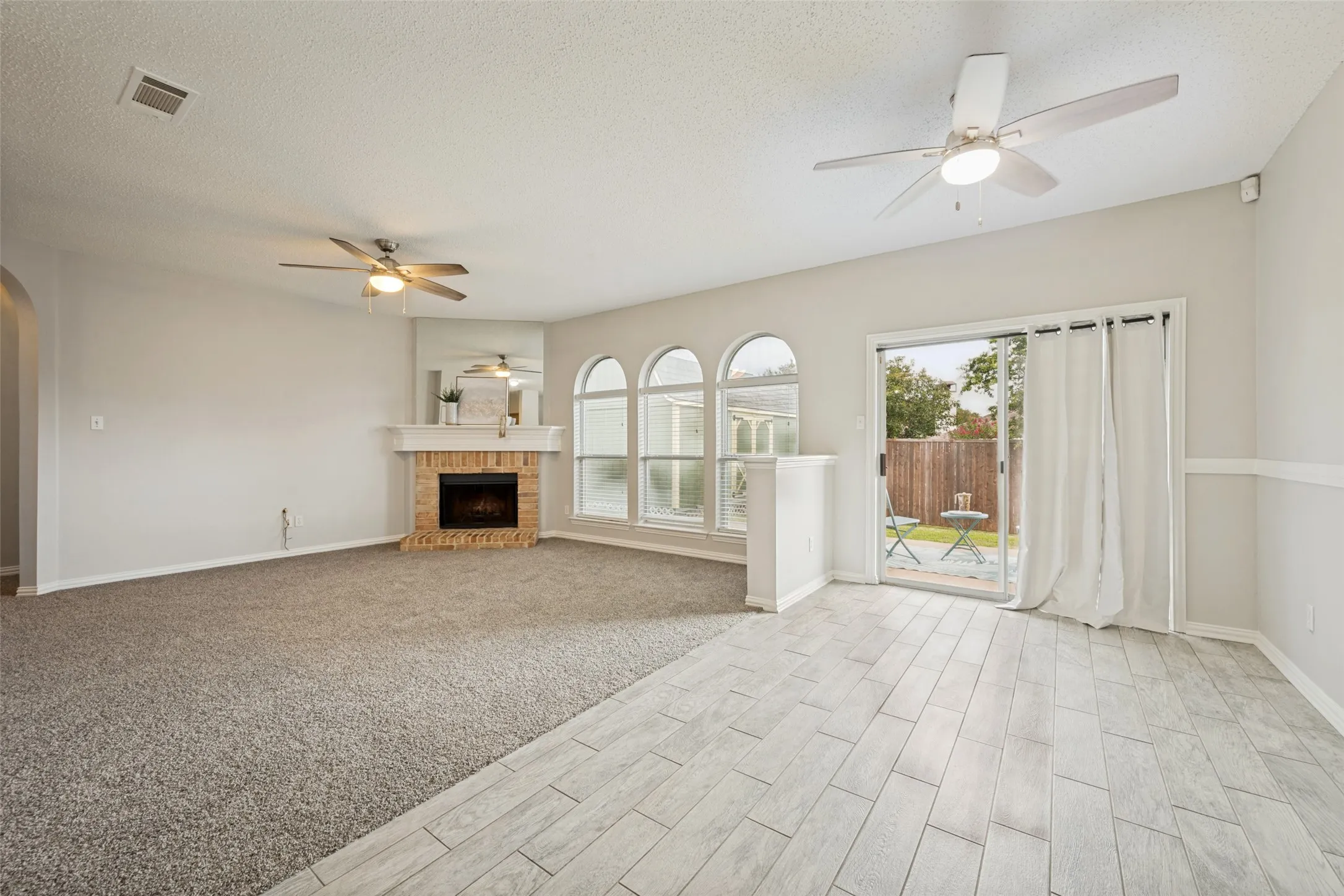 Living area featuring a brick-surround fireplace with a mantel, multiple arched windows, and a sliding glass door