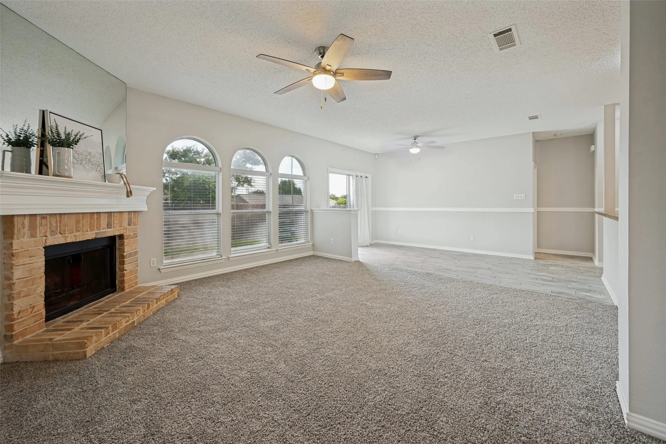 Spacious living area featuring a brick fireplace with a white mantel, multiple arched windows, and soft gray carpeting
