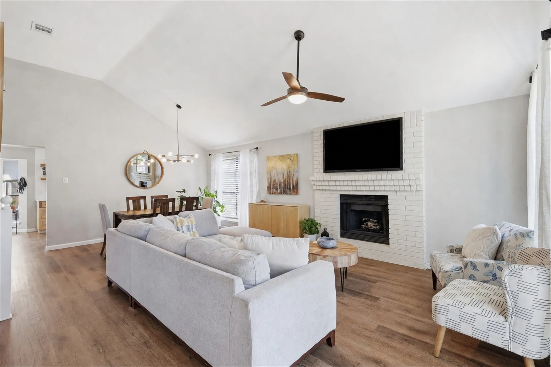 Expansive living area featuring vaulted ceilings, wood-finish flooring, and a white brick fireplace with a built-in mantel