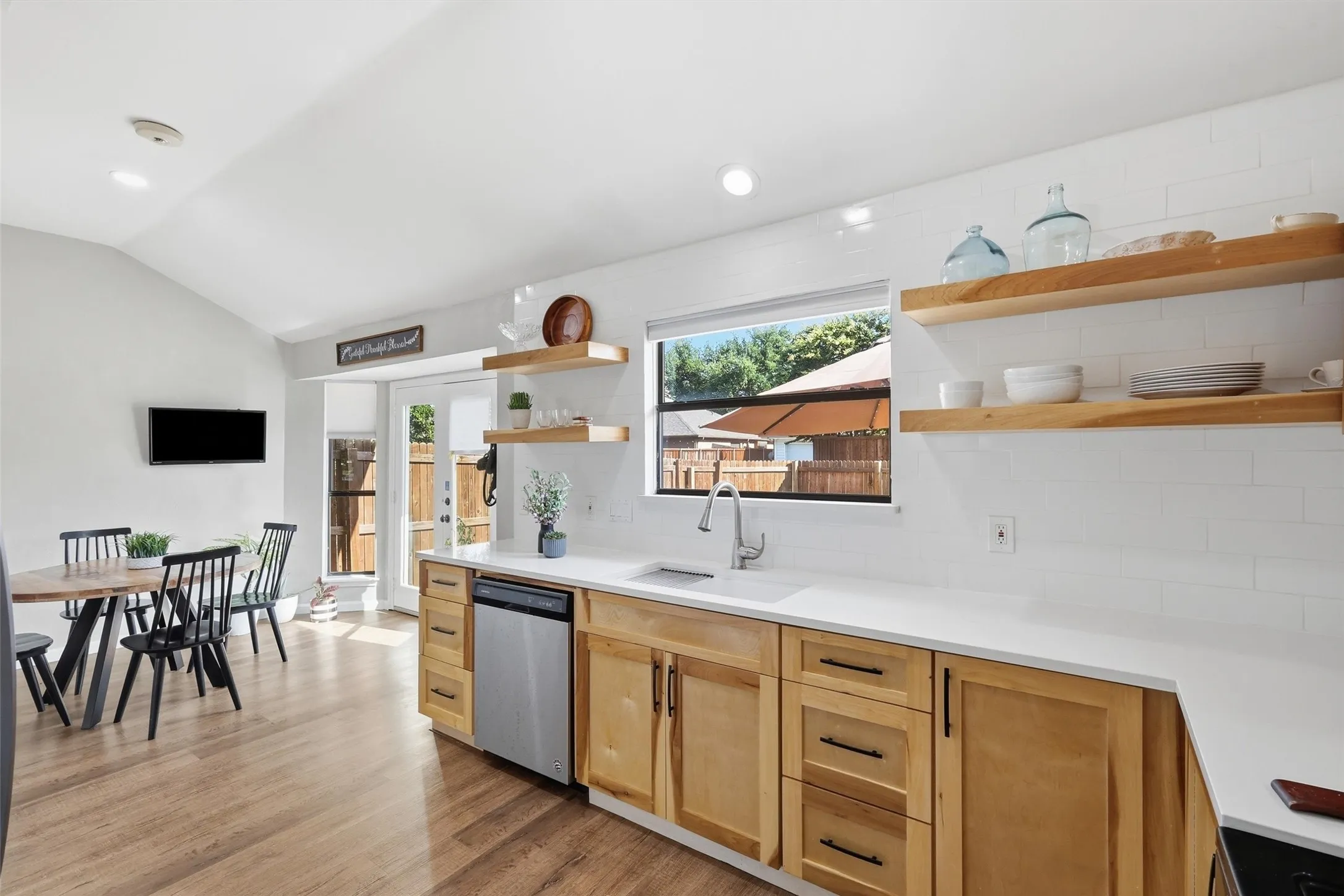 Open-concept kitchen featuring light wood cabinetry, white countertops, white subway tile backsplash, and a stainless steel dishwasher