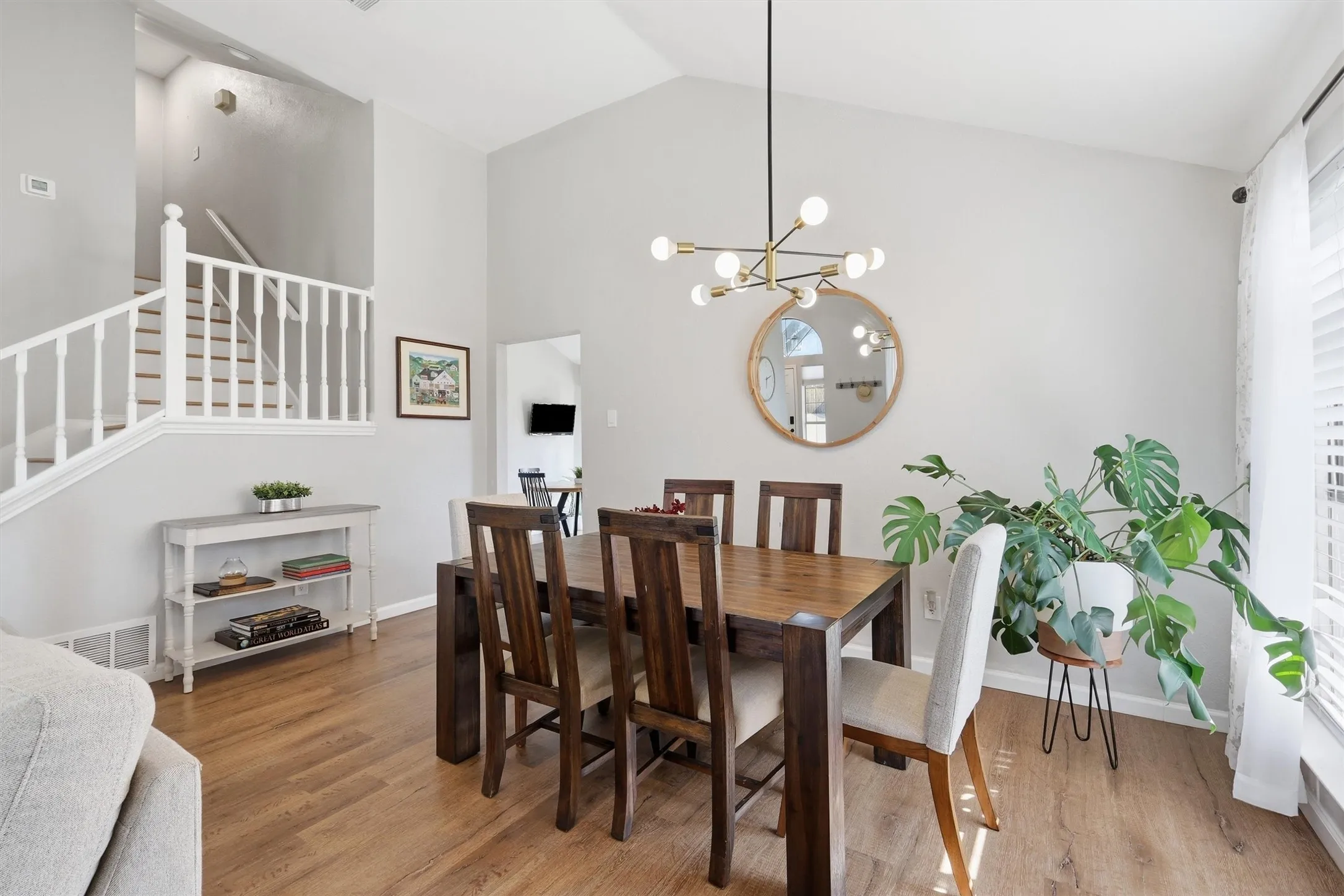 Dining area featuring vaulted ceilings, wood-finish flooring, a modern chandelier, and a prominent round mirror