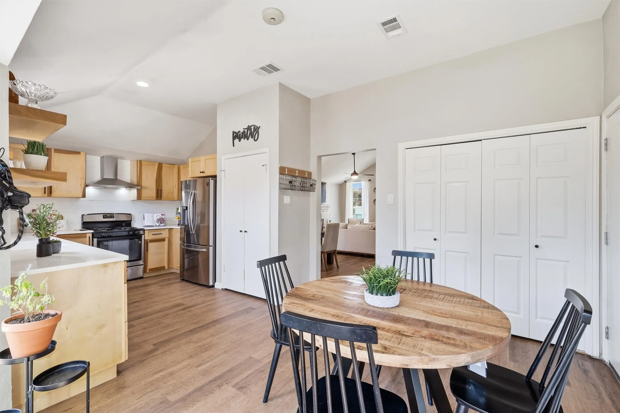 Kitchen and dining area featuring wood-finish flooring, light wood cabinetry, stainless steel appliances, and a vaulted ceiling