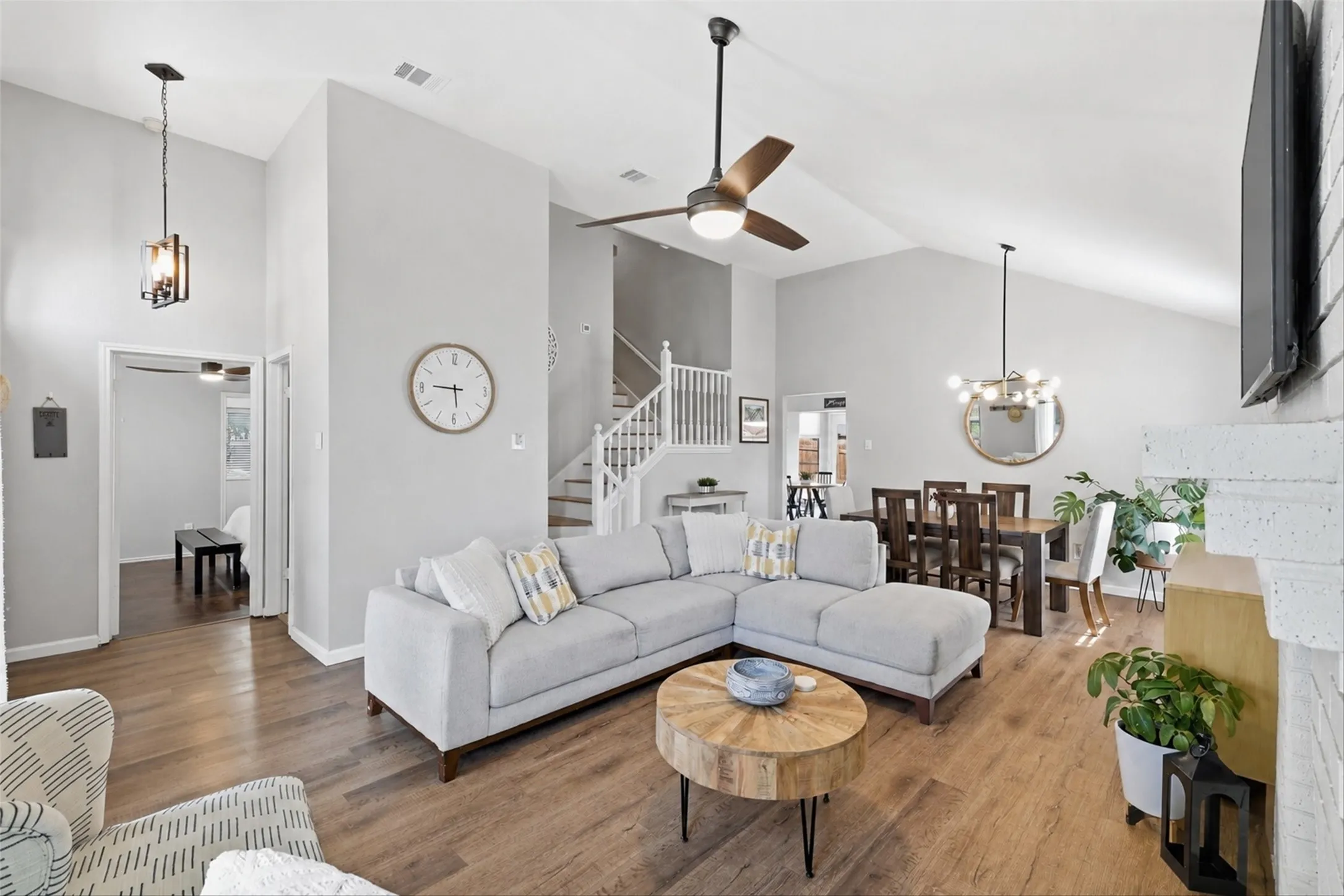 Spacious living area featuring vaulted ceilings, wood-finish flooring, a modern ceiling fan, and a painted brick fireplace surround