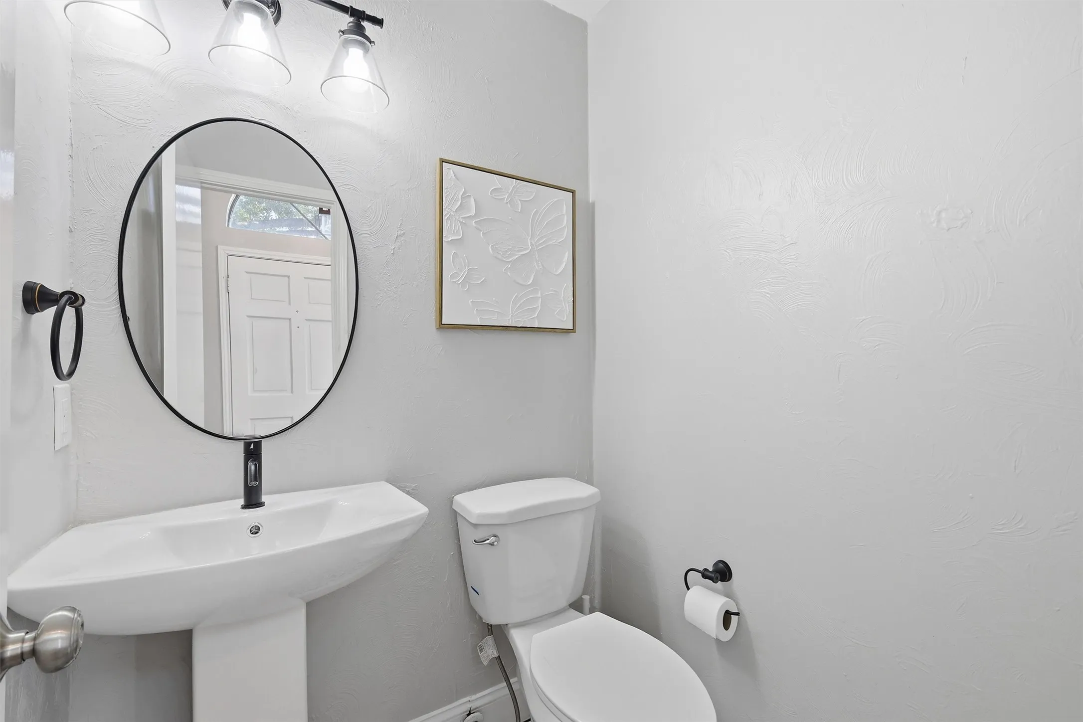 Modern powder room featuring a pedestal sink with a black single-handle faucet, a black-framed oval mirror, and a three-light vanity fixture