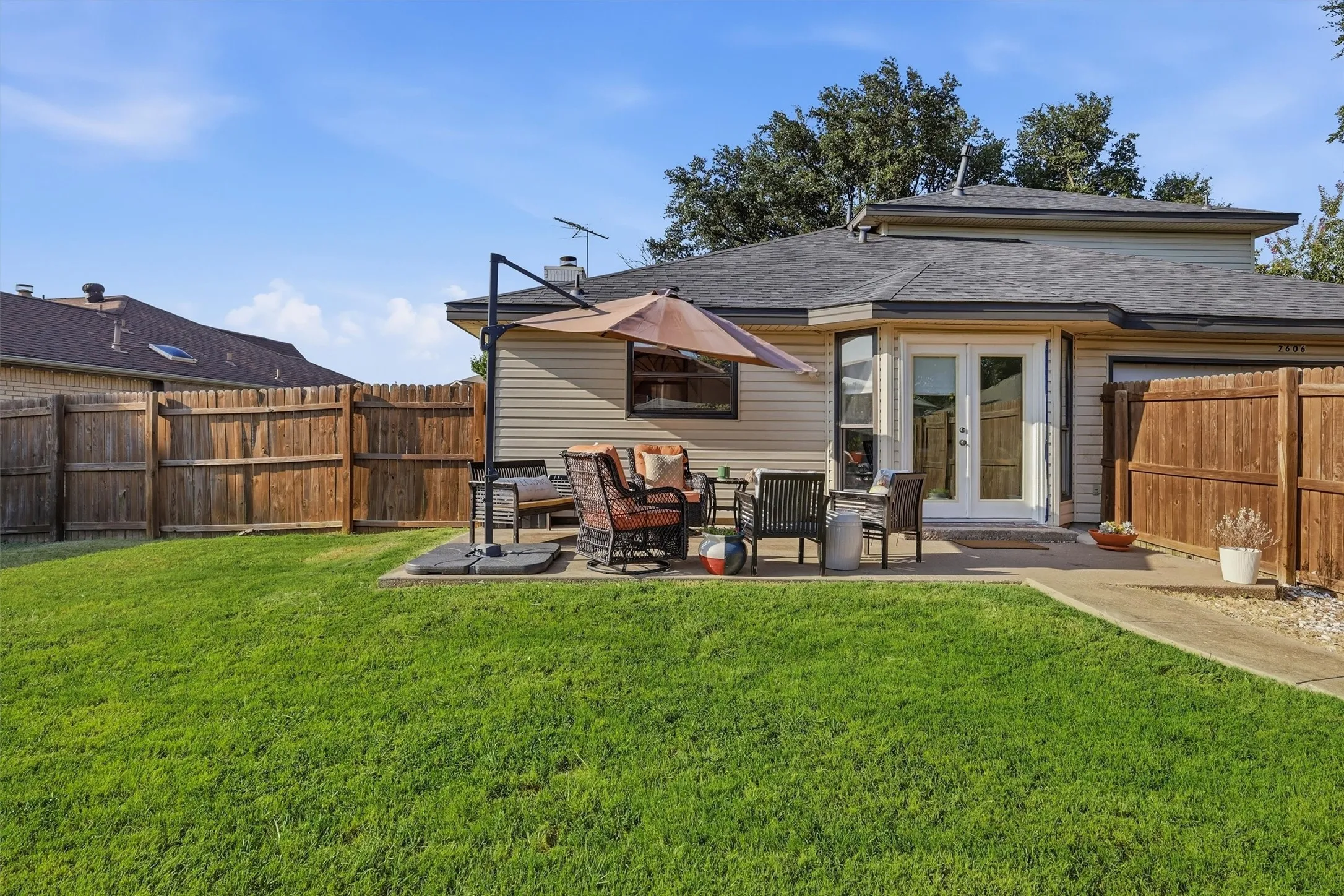 Expansive lawn area featuring a concrete patio, wood privacy fencing, and double glass French doors