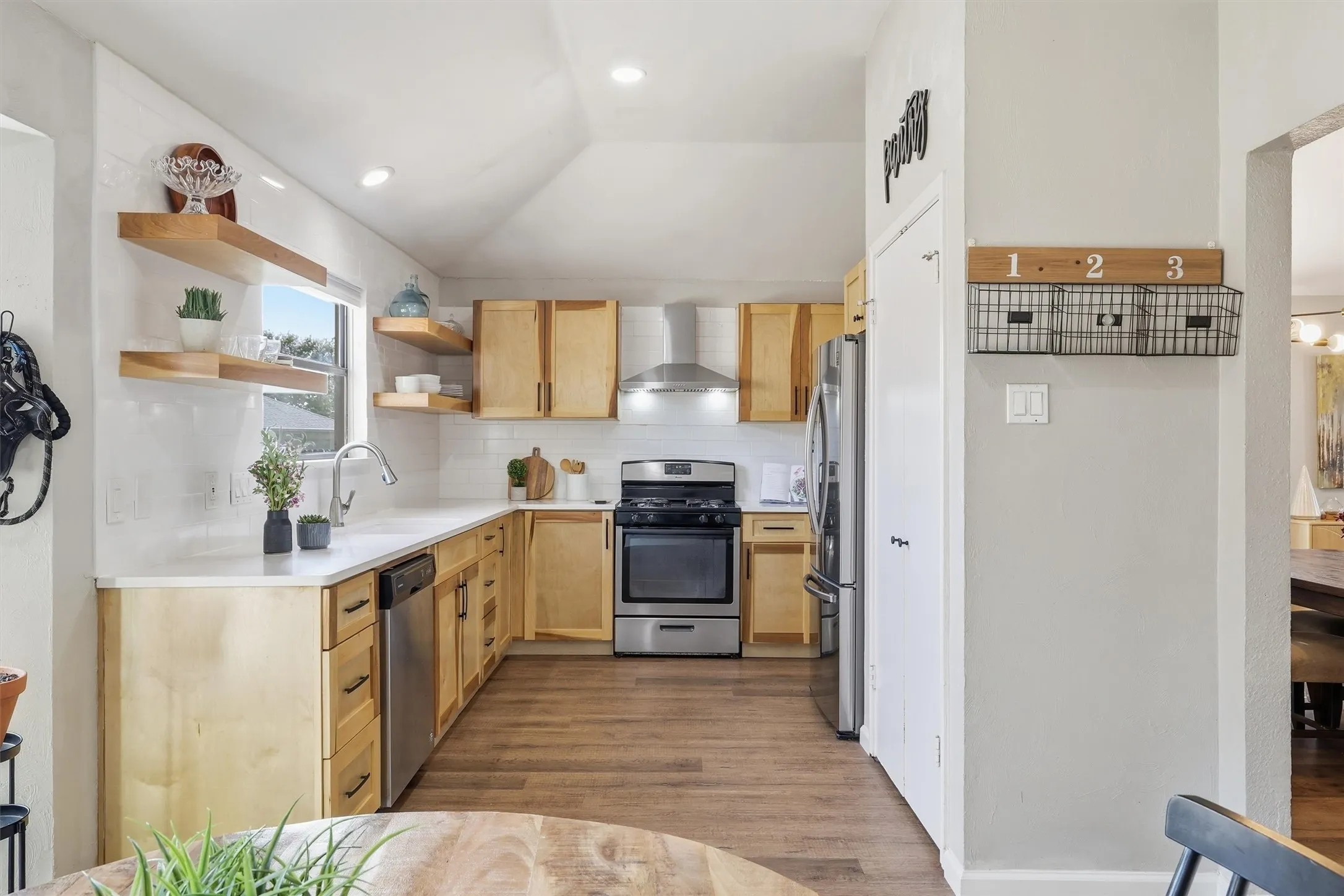 Kitchen featuring wood-finish flooring, light wood cabinetry, stainless steel appliances, a white subway tile backsplash, and recessed lighting