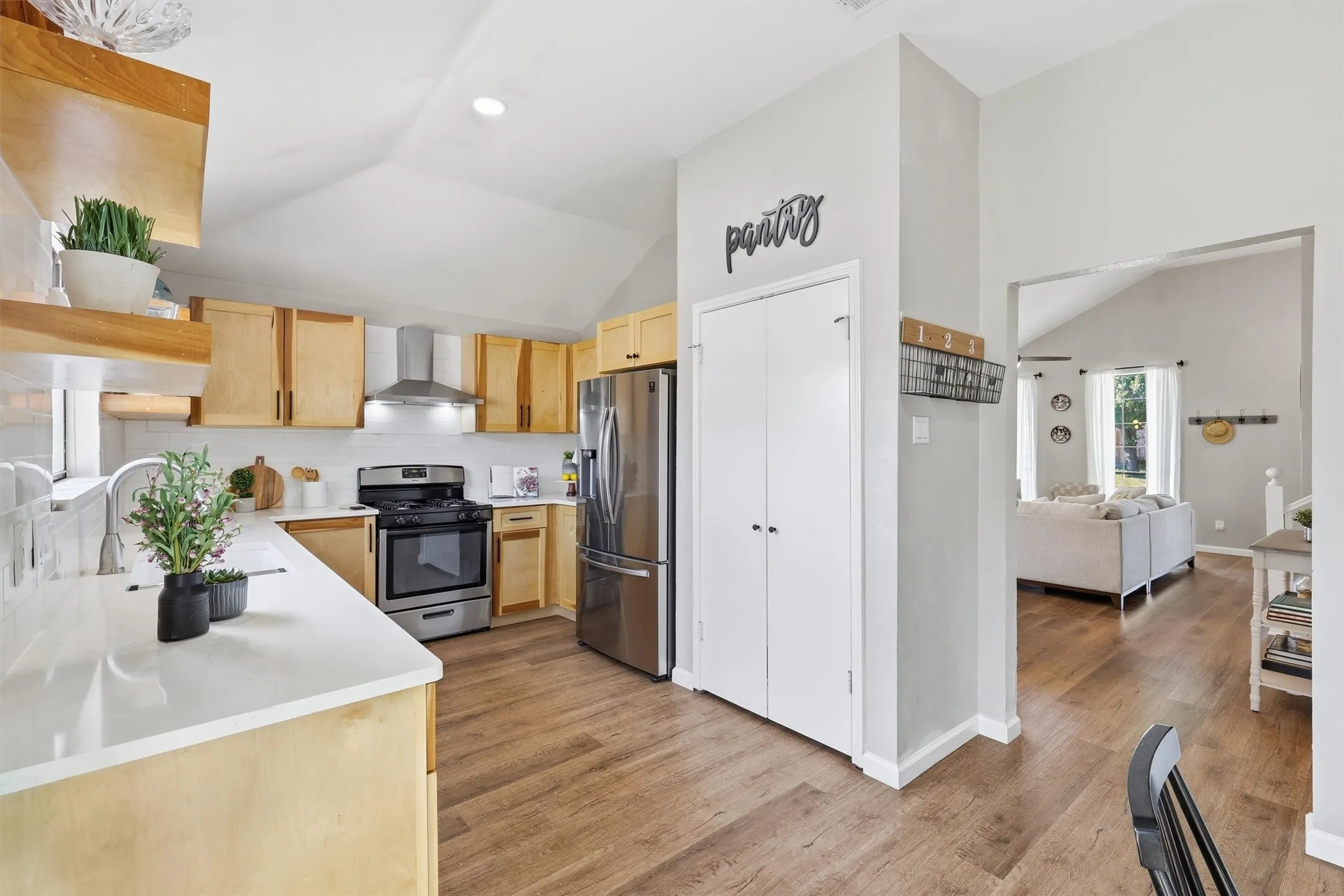Kitchen featuring vaulted ceilings, light wood cabinetry, stainless steel appliances, white countertops, and wood-finish flooring