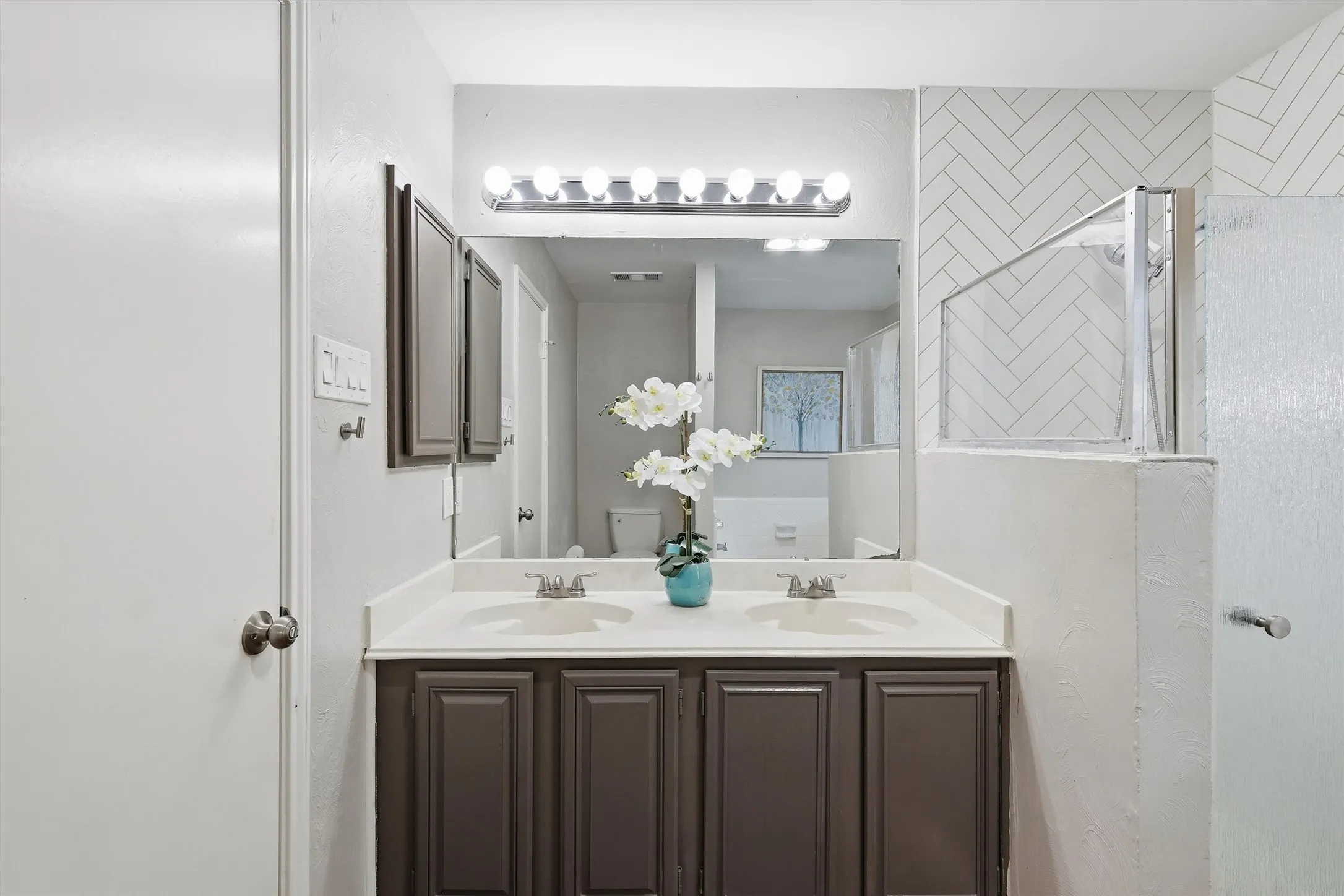 Bathroom vanity featuring dual sinks, white countertop, and dark wood-finish cabinetry