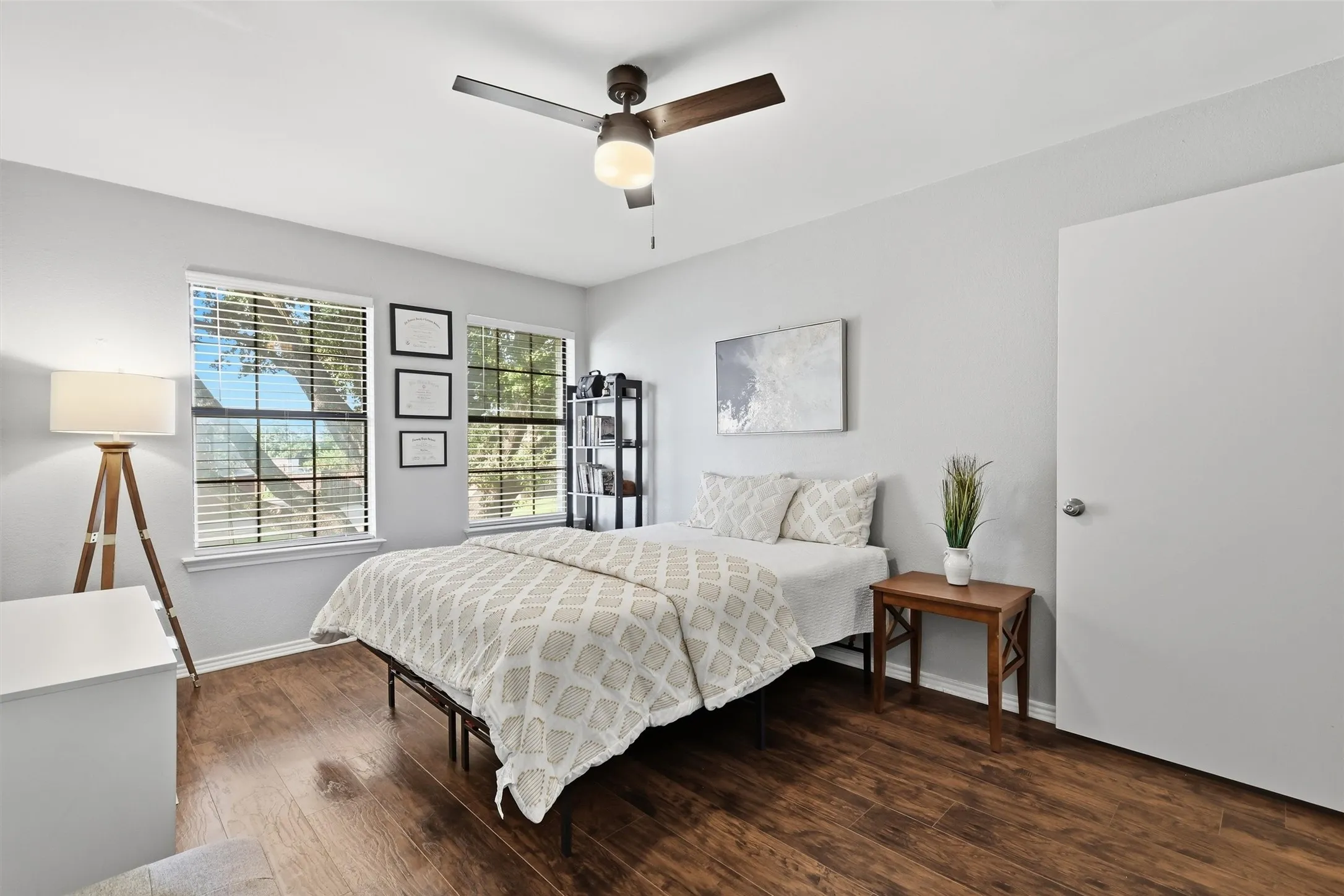 Room featuring wood-finish flooring, light gray walls, a ceiling fan with integrated lighting, and two large windows with blinds