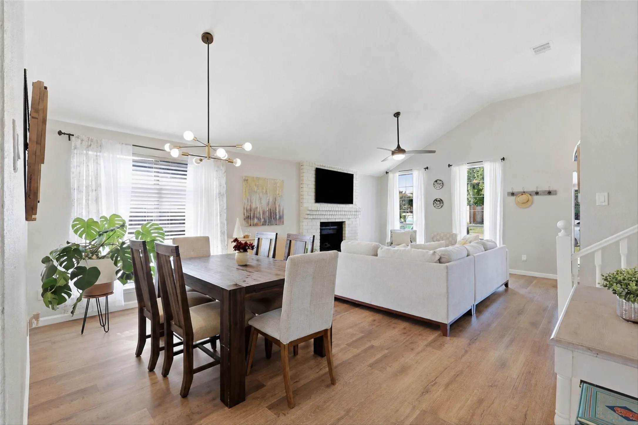 Open-concept living space featuring wood-finish flooring, vaulted ceiling, and a prominent brick-clad fireplace