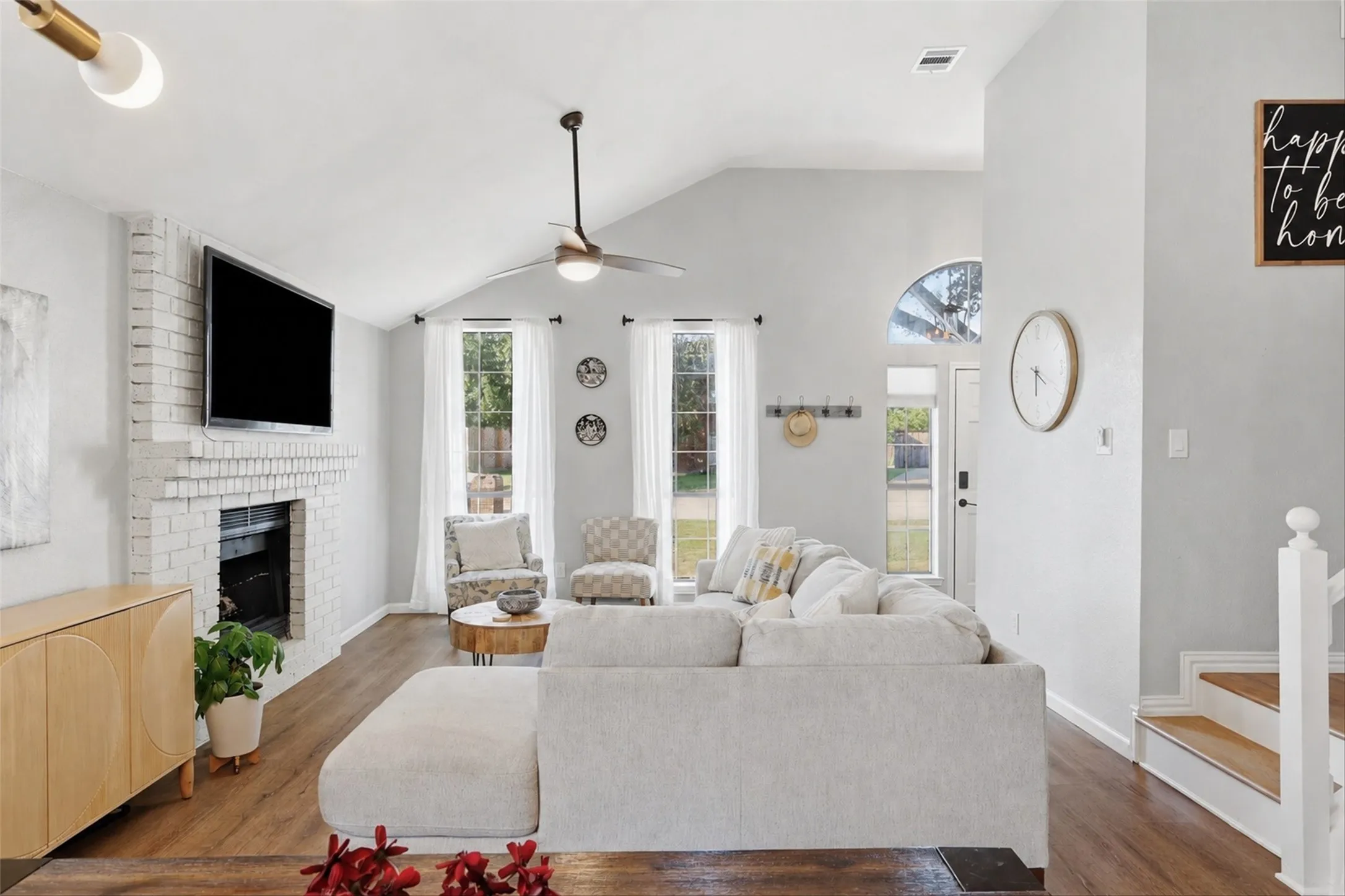 Vaulted ceiling living area featuring wood-finish flooring, a painted brick fireplace, and multiple windows